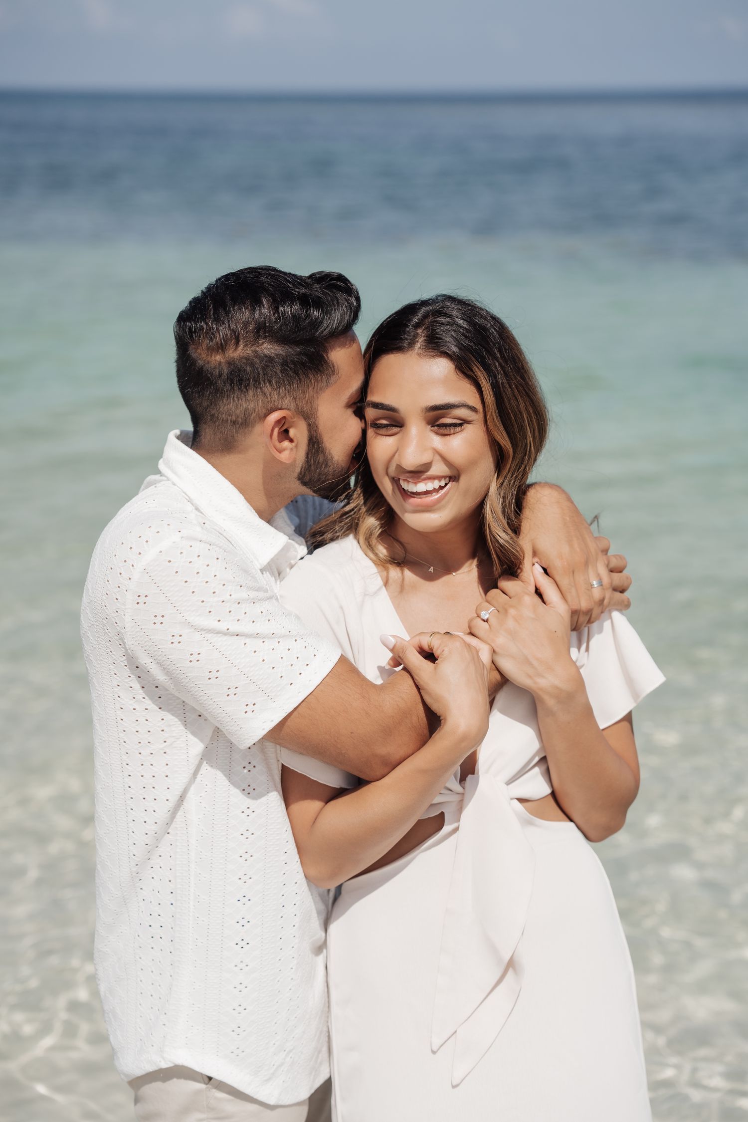 A loving embrace between a couple on a pristine beach with crystal clear waters.