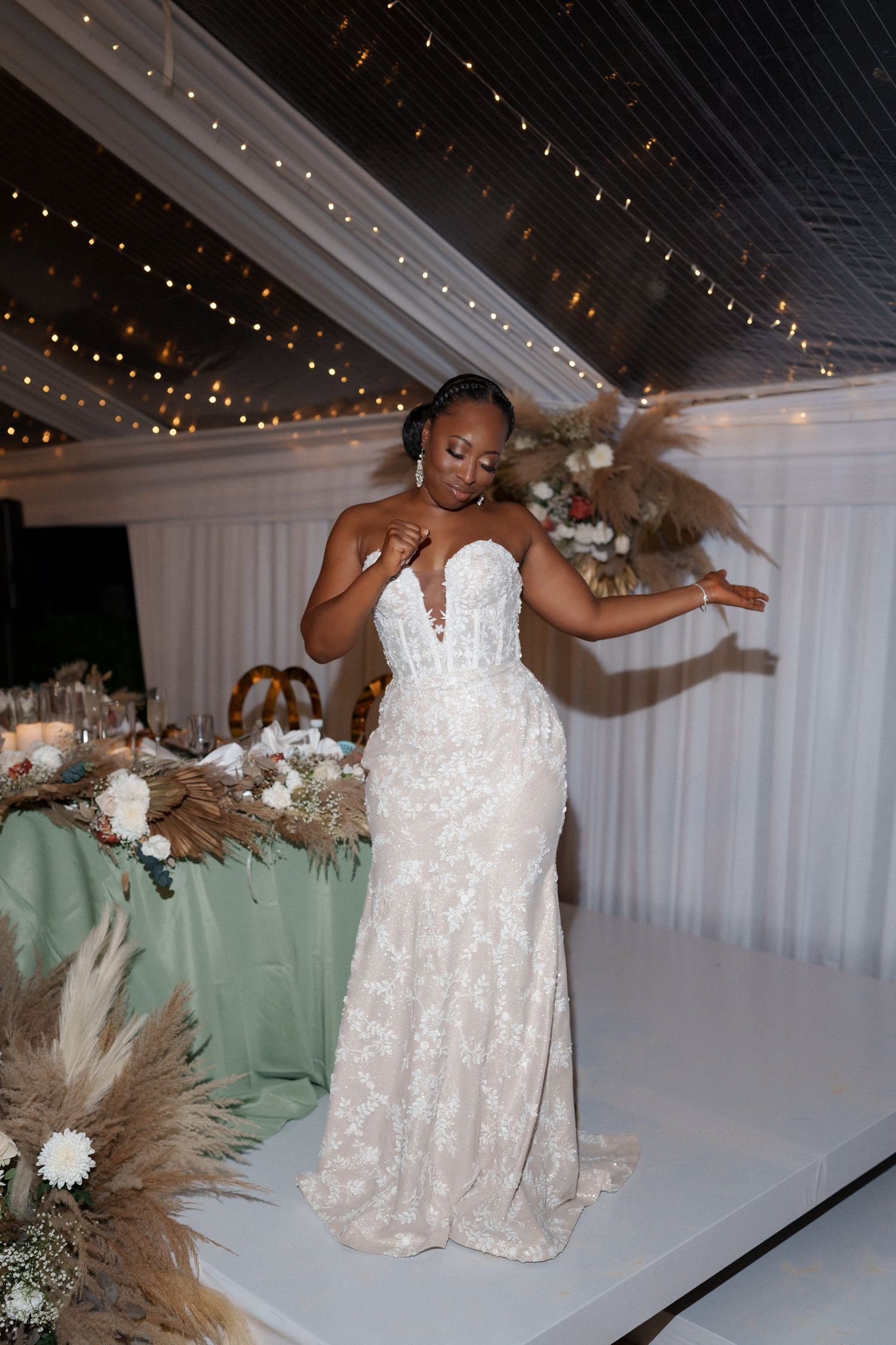 A bride in a stunning lace white wedding gown dances joyfully under twinkling lights.