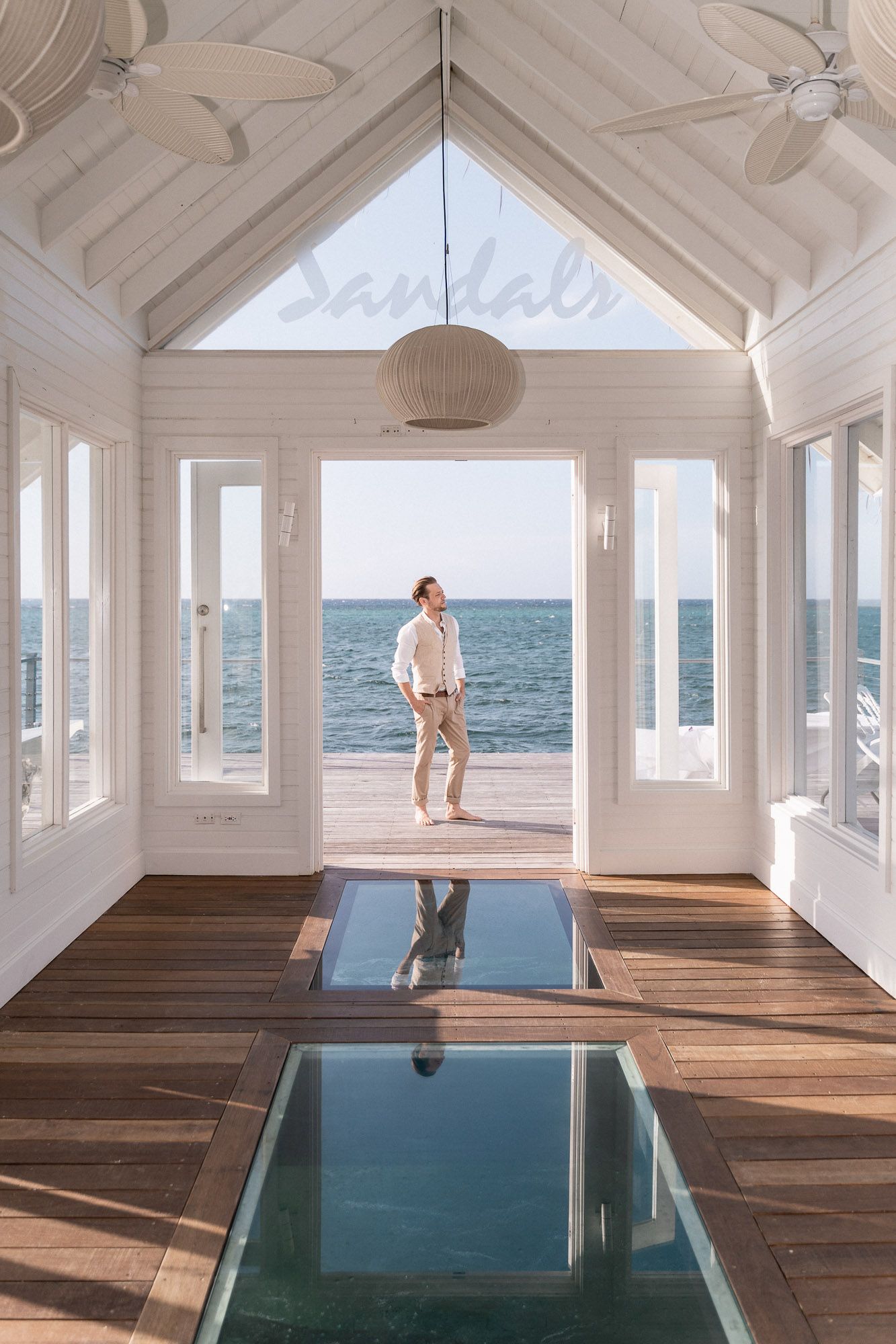 Interior of a white beach house with ocean view through large windows and wood floors.