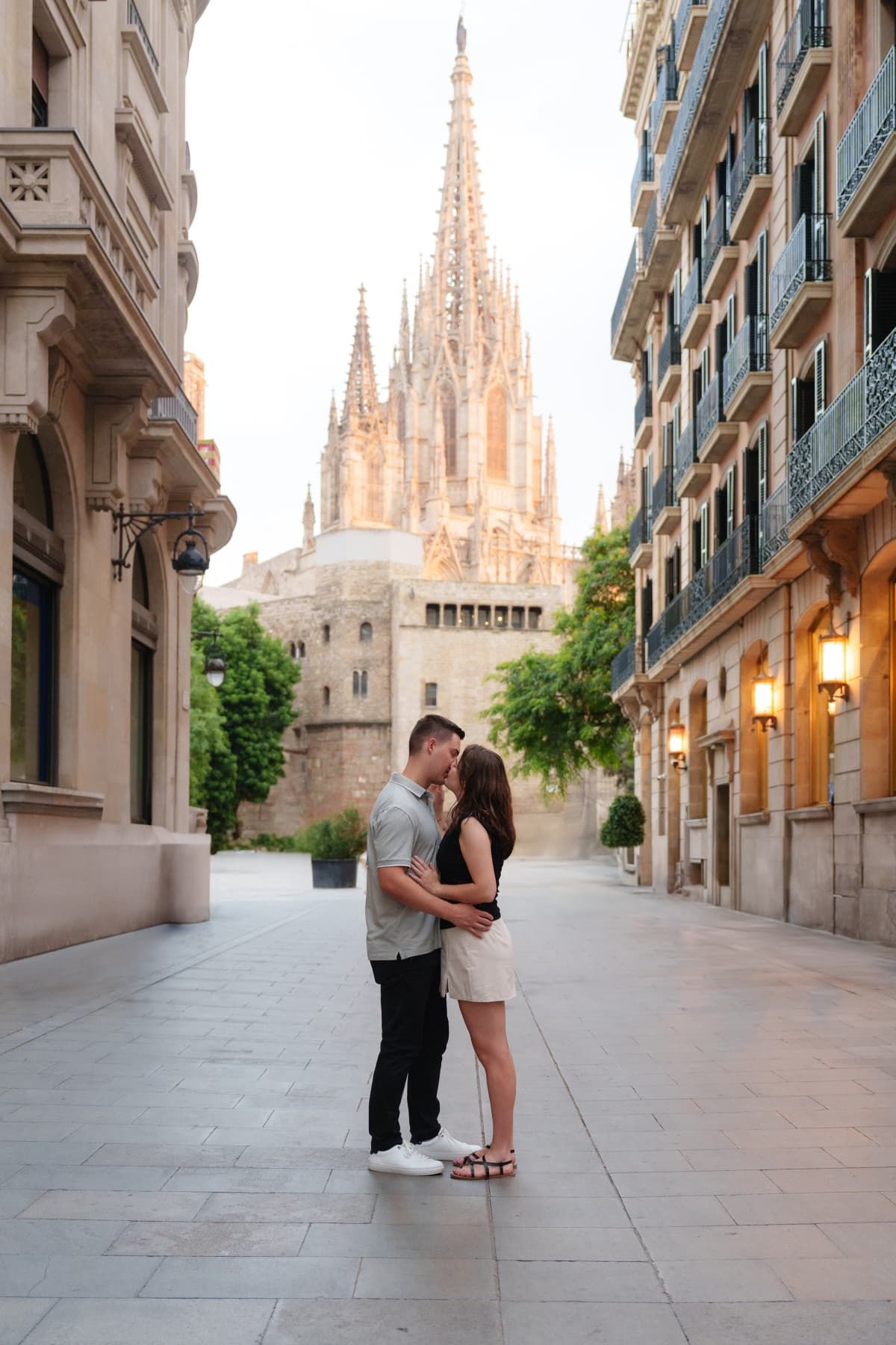 A couple shares a romantic moment in front of Barcelona Cathedral's Gothic spires during golden hour.