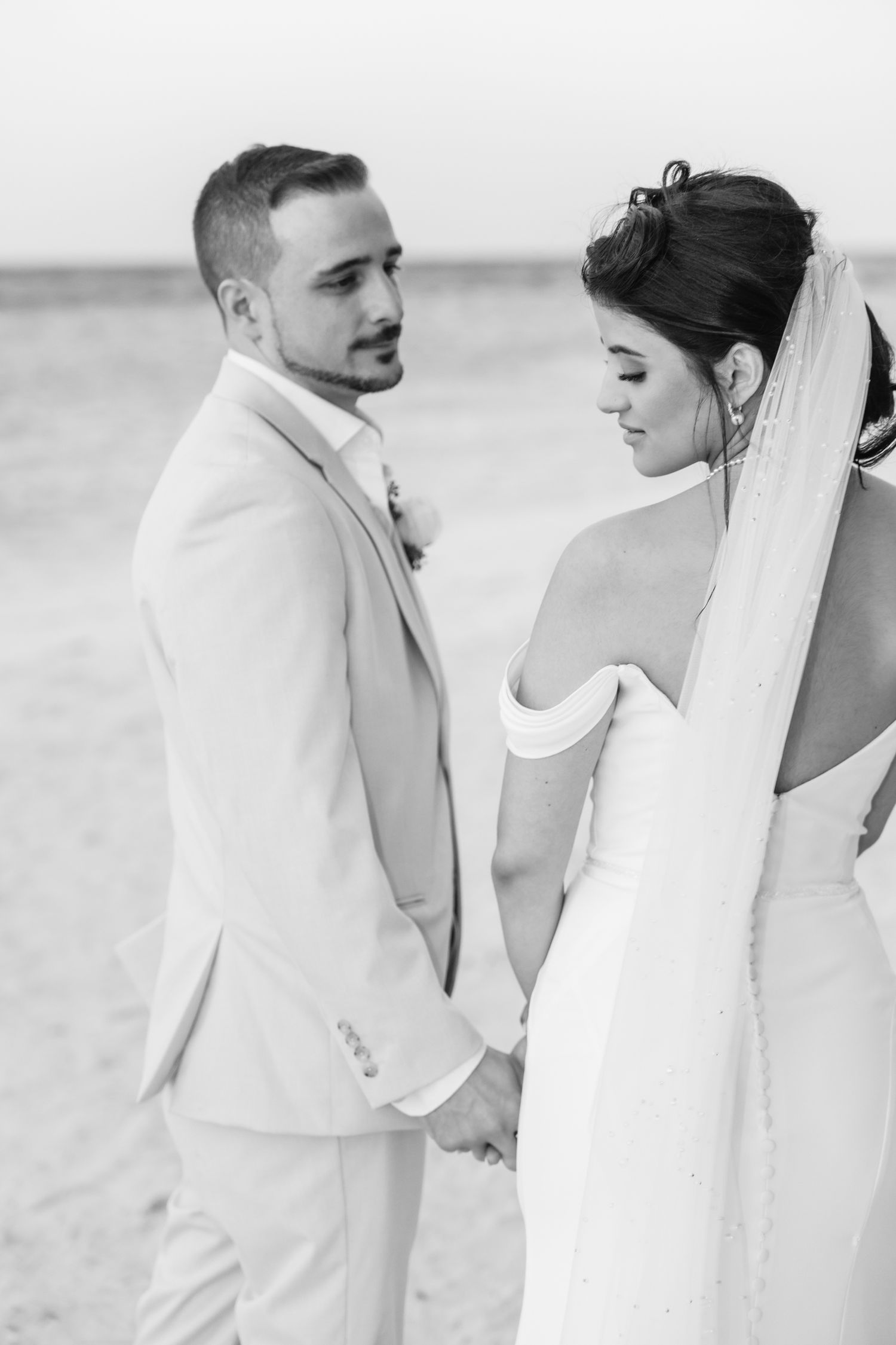 A black and white portrait of a couple in wedding attire on a beach.