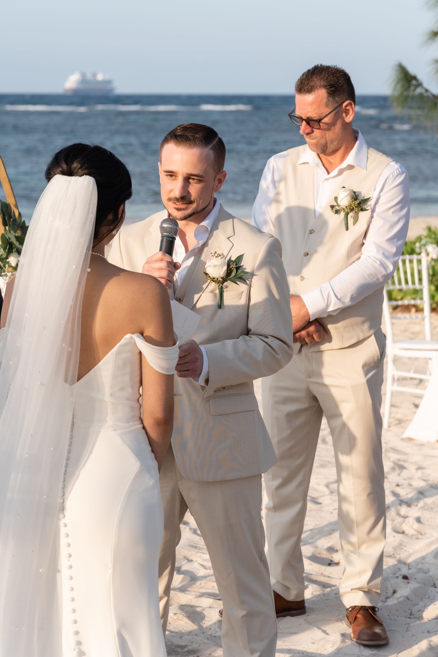 A beach wedding ceremony taking place with attendees in light colored attire and the ocean visible in the background.