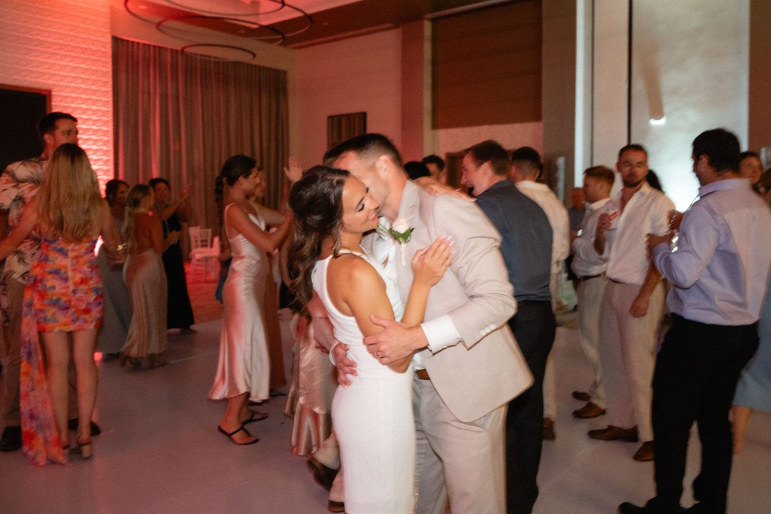 Couples dancing at an elegant reception with ambient pink lighting.