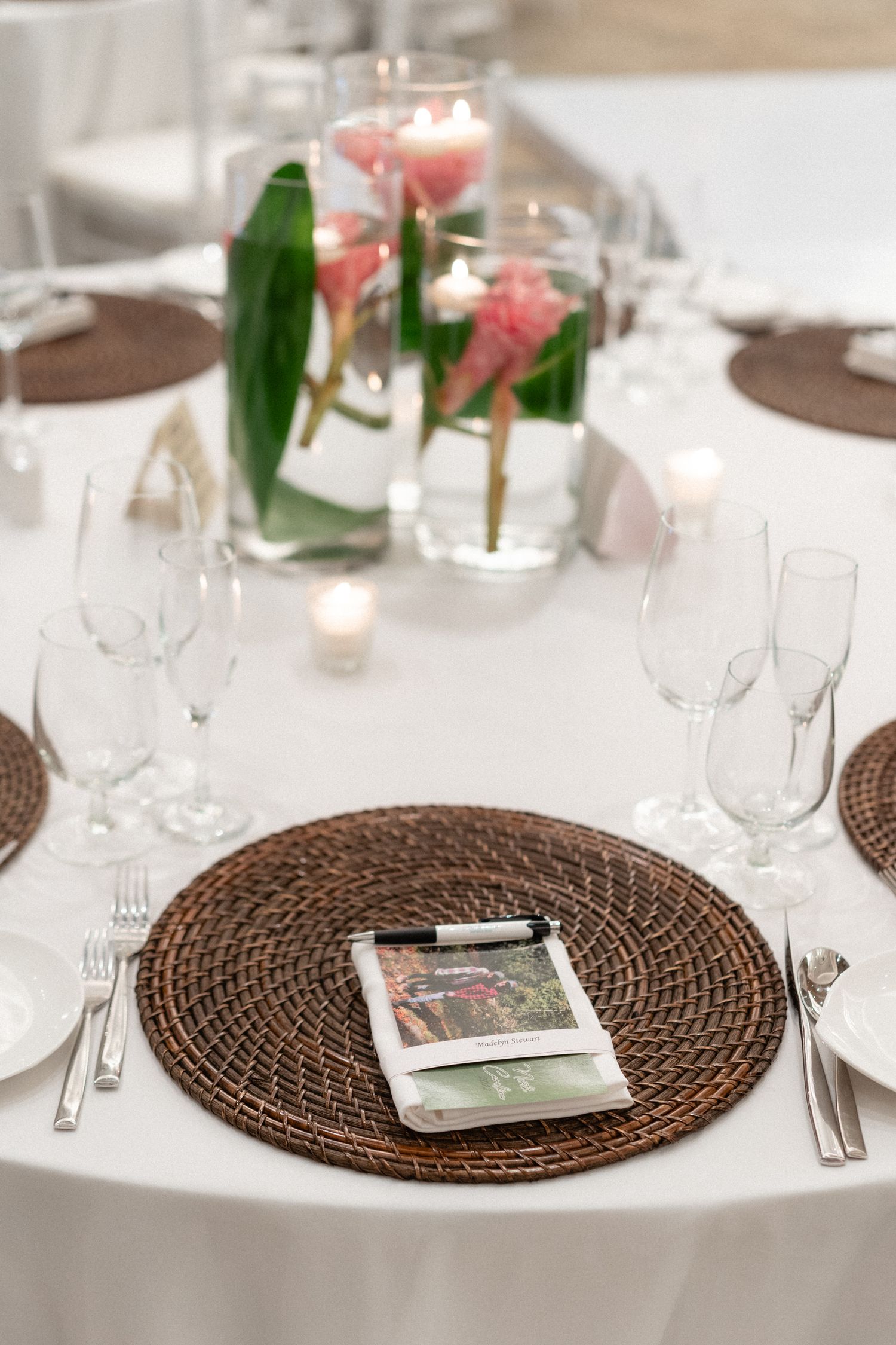 Elegant wedding table setting with rattan charger, pink floral centerpiece and wine glasses.