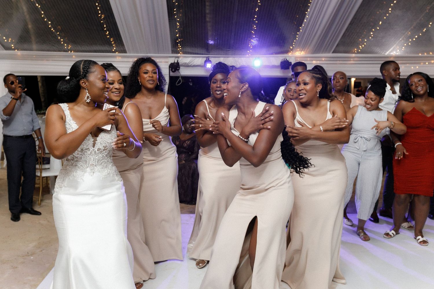 Bridesmaids in elegant champagne-colored dresses laugh and celebrate together on the dance floor at a wedding reception.