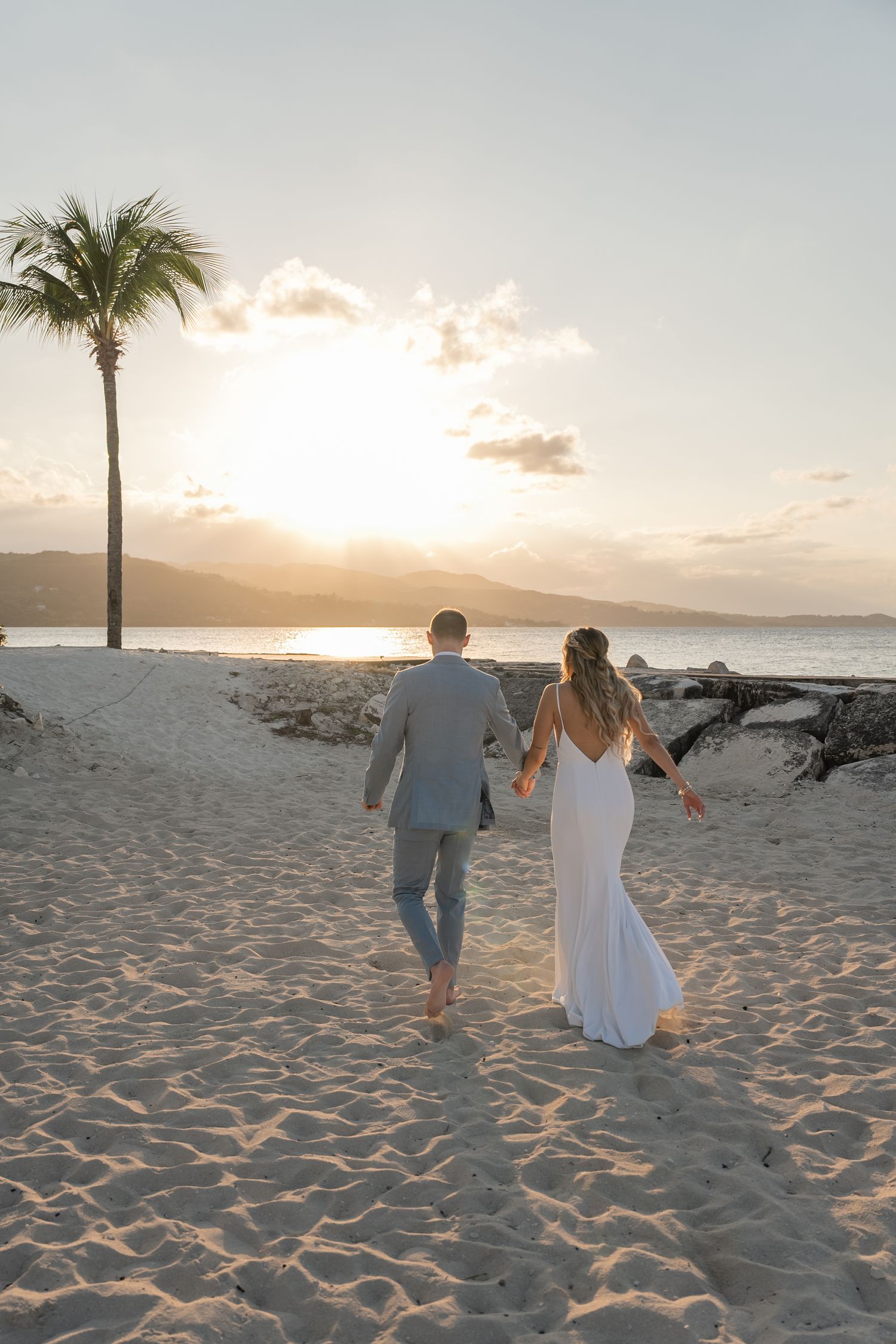 A couple walking barefoot on the beach during golden hour sunset.