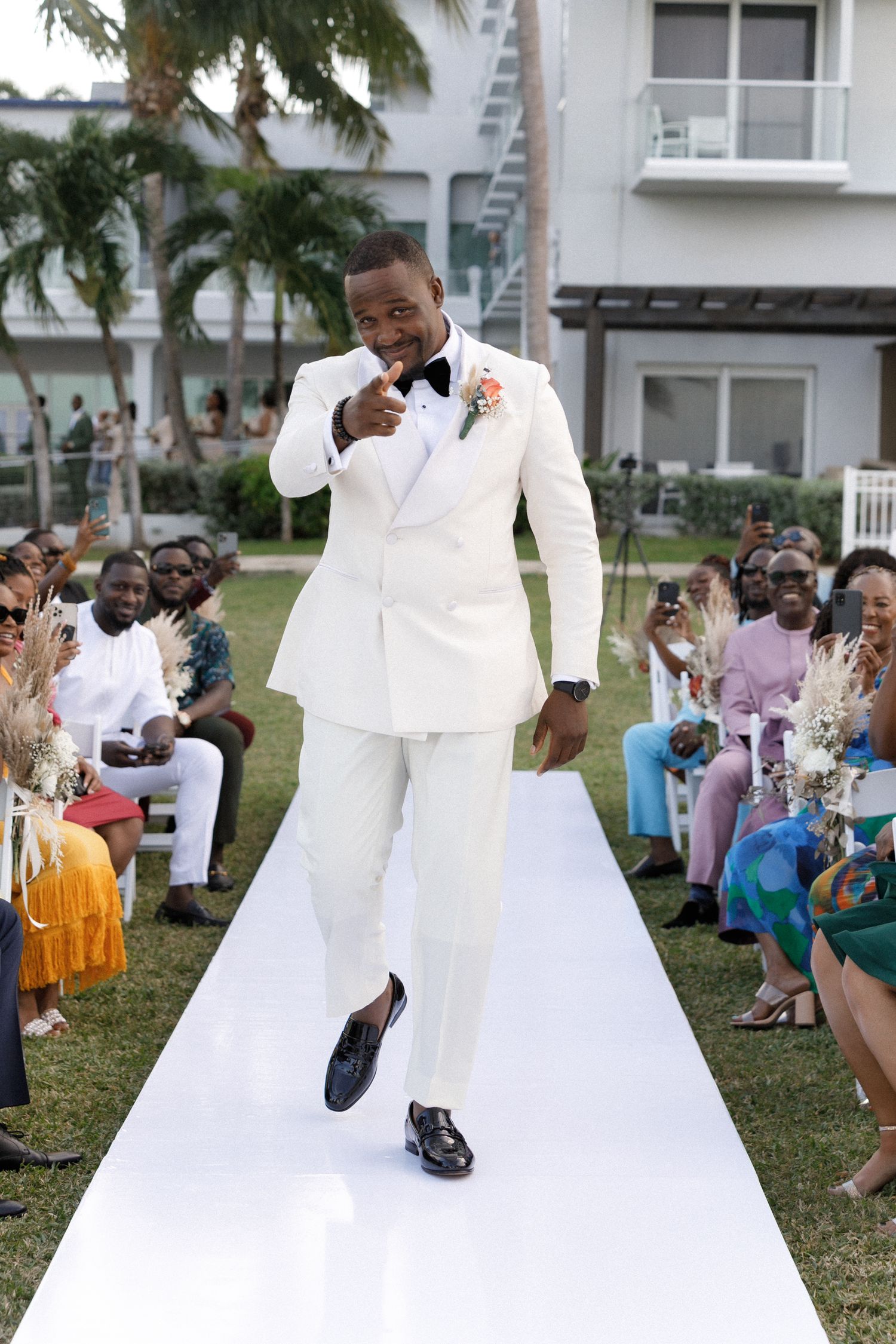 A stylish performer walks confidently down an outdoor white runway wearing a classic white suit.