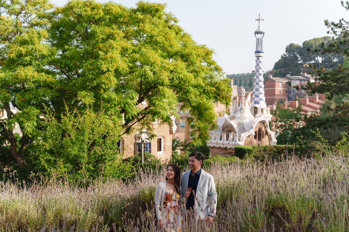 Couple walking through a lush garden path with tall grasses and trees on a sunny summer day.