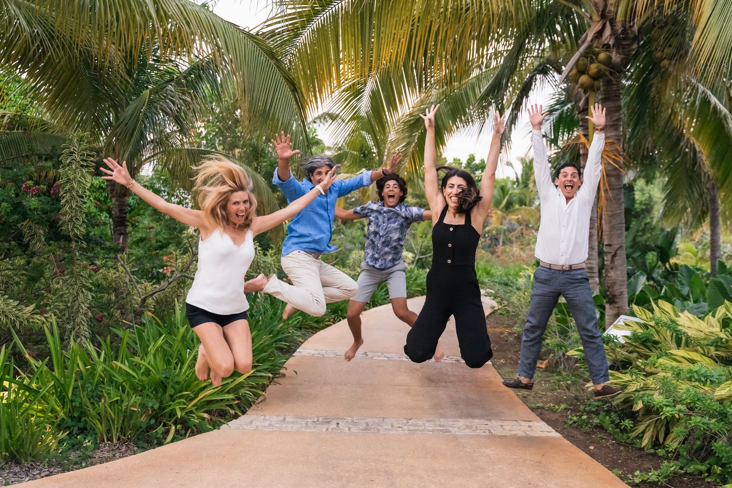 A group of people jumping joyfully on a palm tree-lined pathway in a tropical setting.