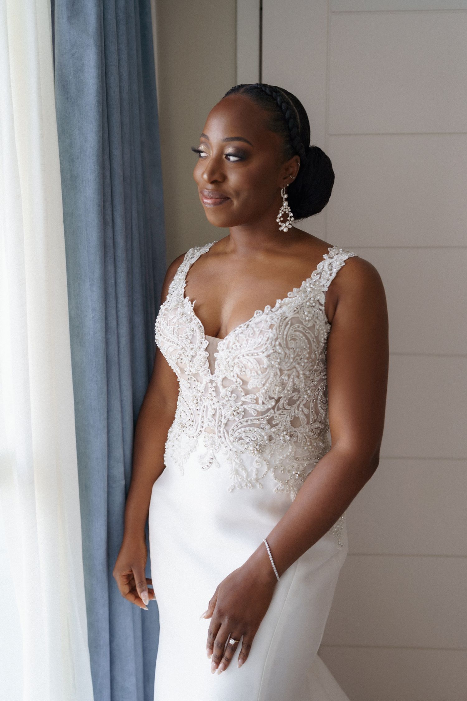 Beautiful wedding gown with delicate lace detail and elegant silhouette by a window.