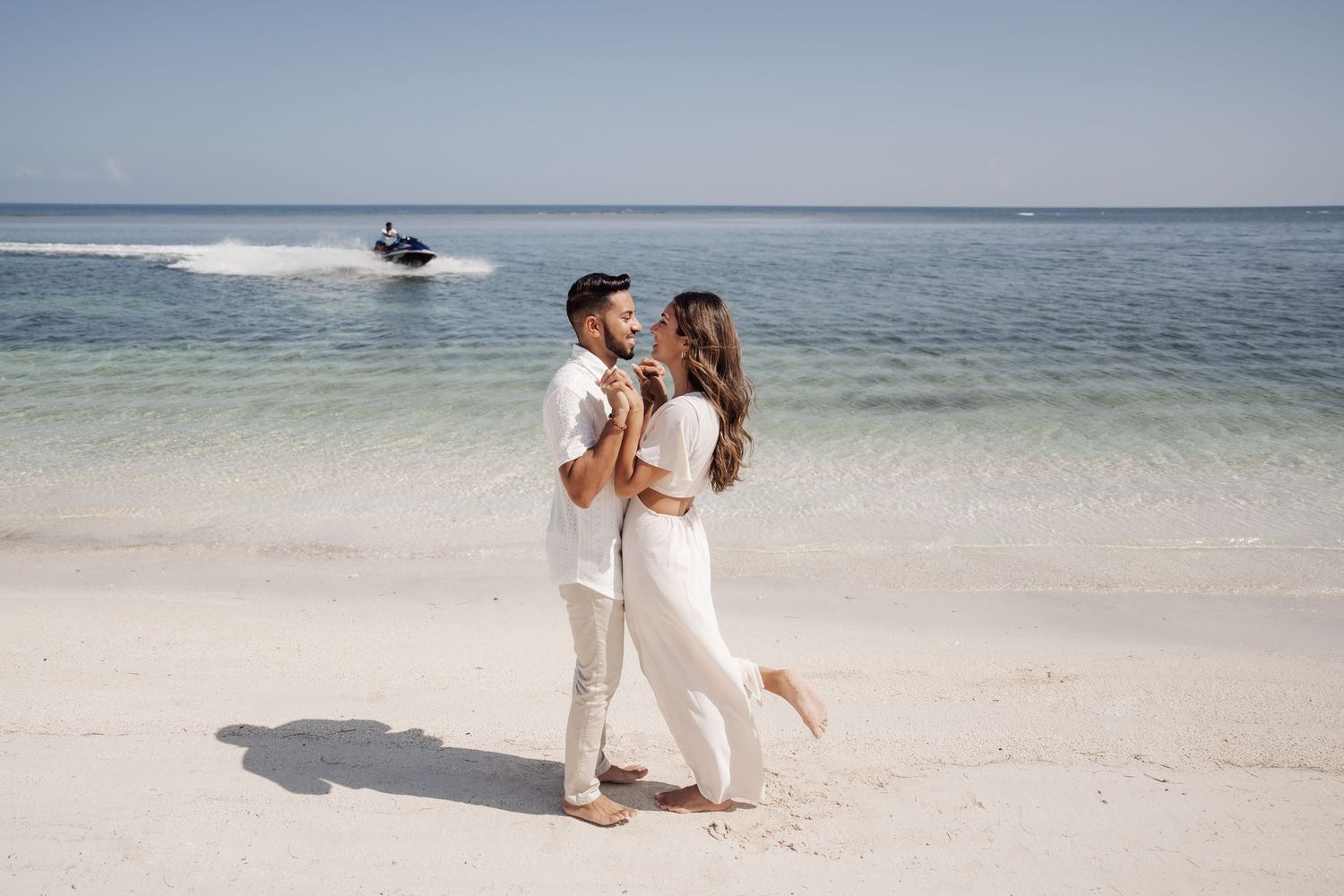 Two people dancing together on a white sandy beach with turquoise waters in the background.