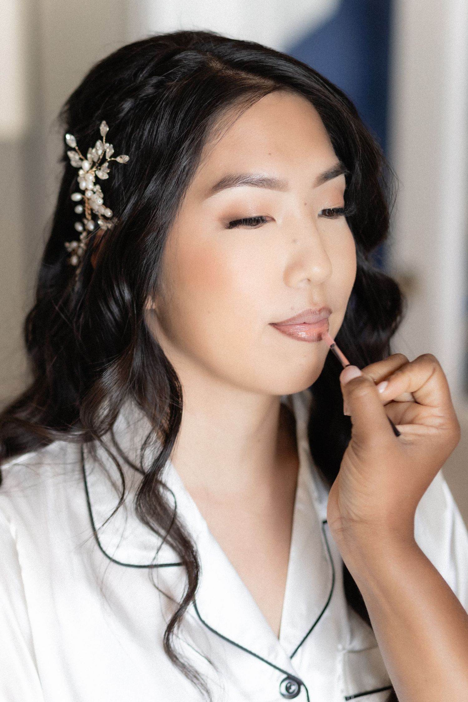 Close up of a bride getting professional makeup done while wearing a white silk robe and crystal hair accessory.