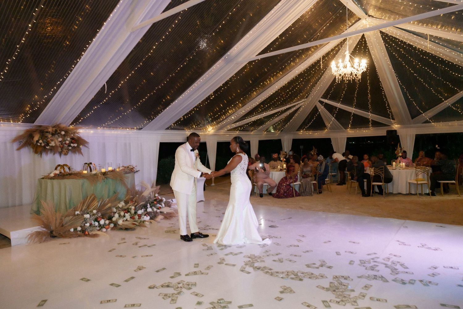 First dance in an elegant white tent reception with string lights and romantic atmosphere.