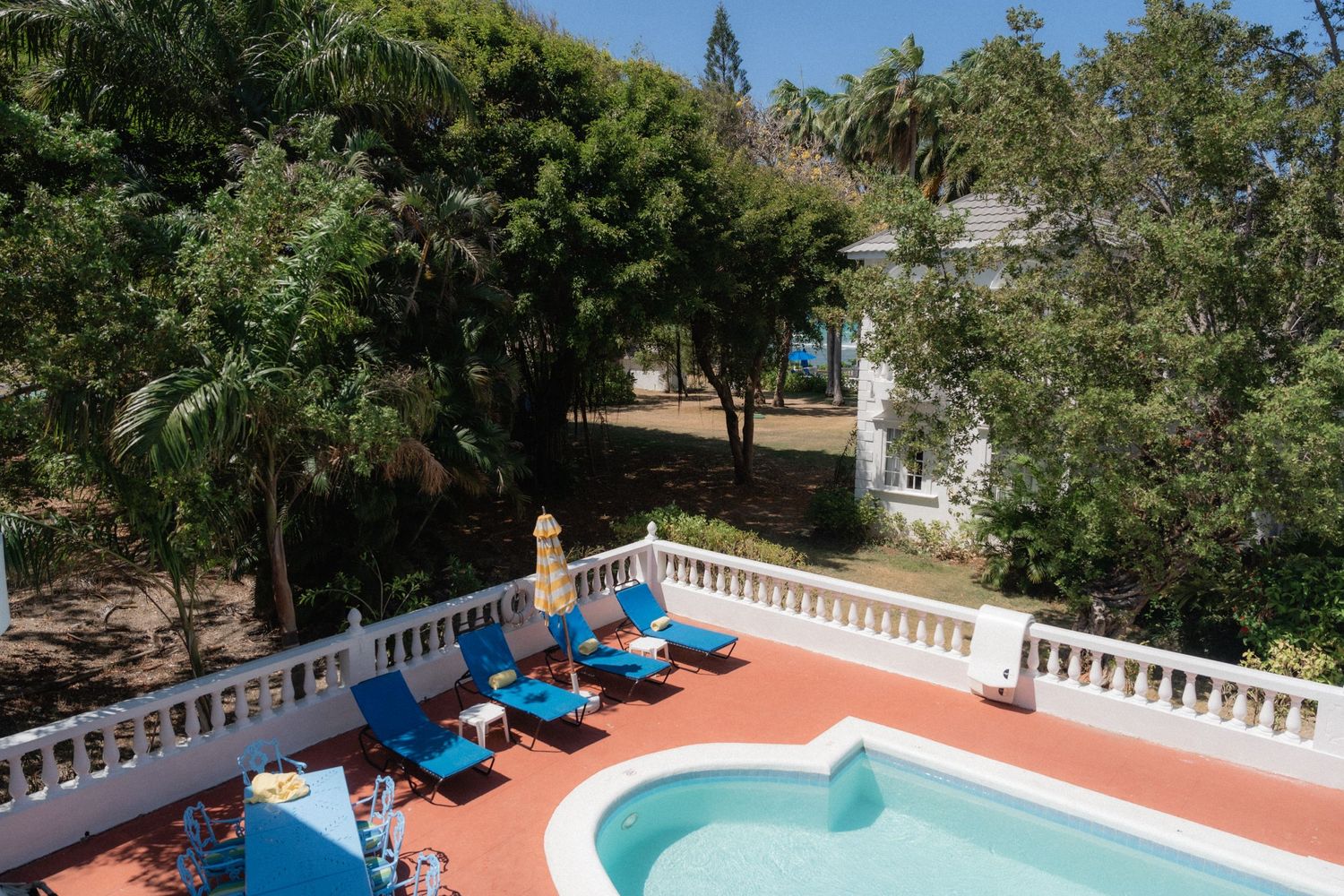 Aerial view of swimming pool with blue loungers and white balustrade surrounded by lush greenery.