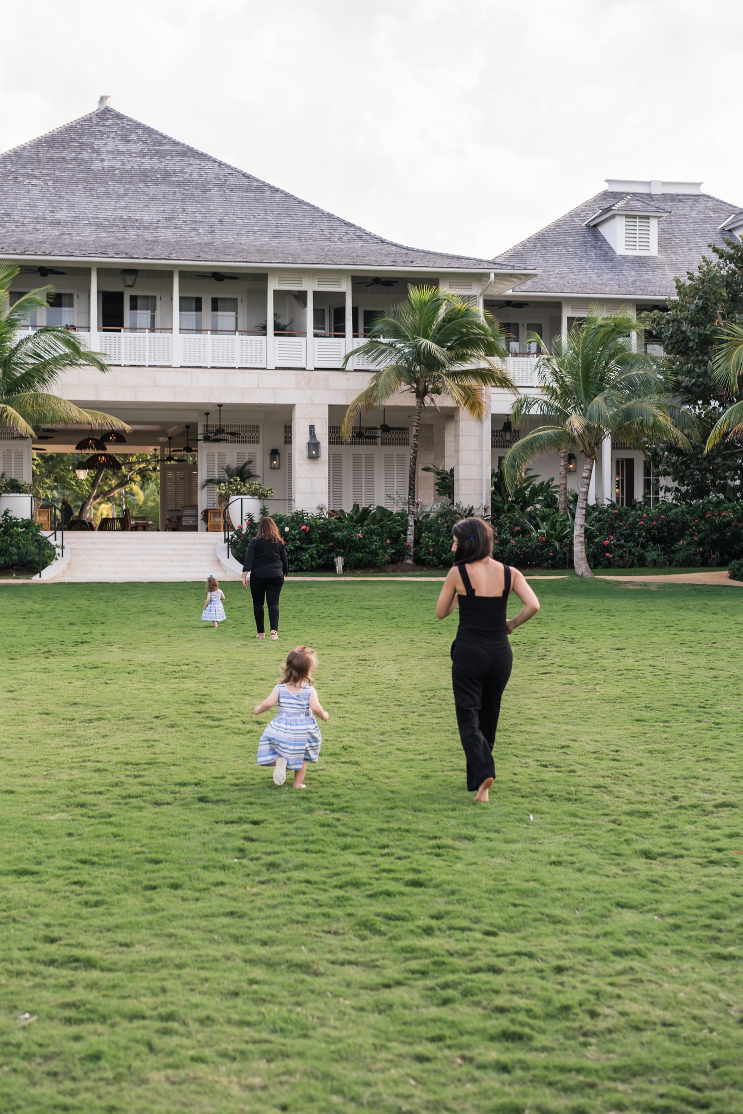 A peaceful scene of people walking across a grassy lawn towards a tropical beach house.