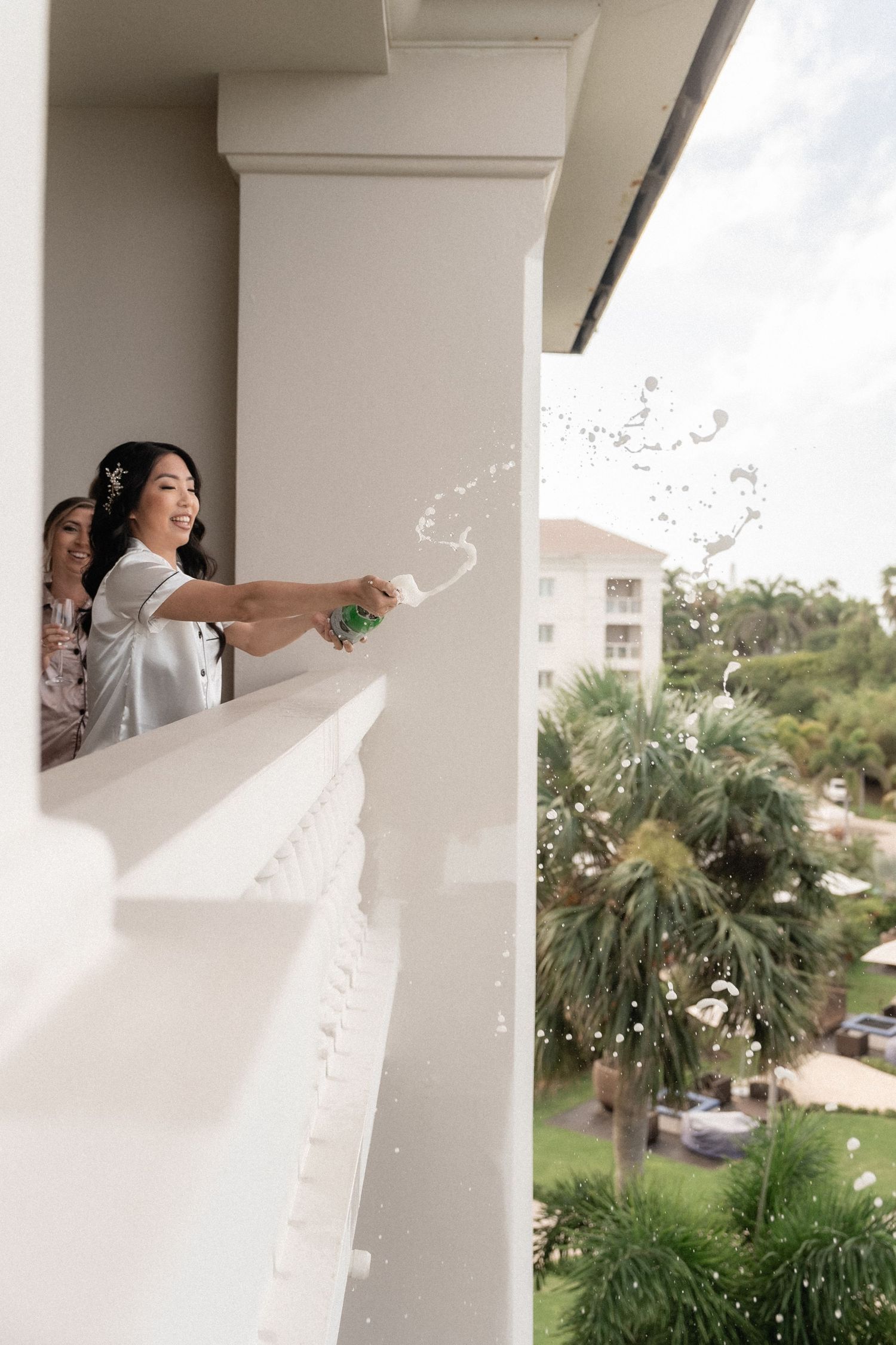 Someone celebrating by popping champagne from a balcony overlooking tropical palm trees.