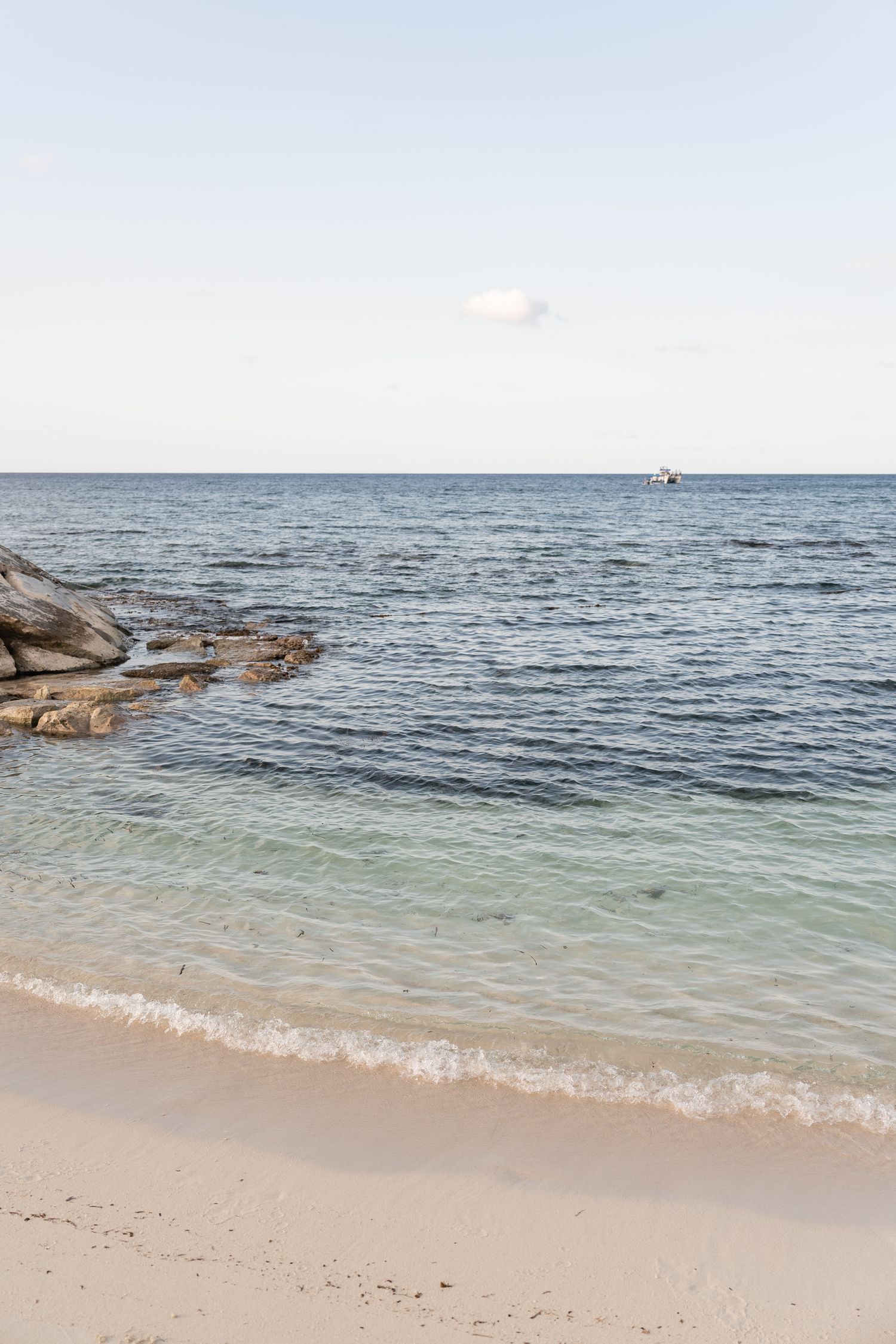 Serene ocean view with rocky outcrop and gentle waves lapping at sandy beach.