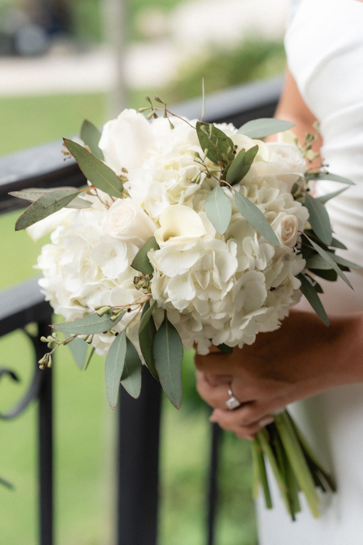 Classic white hydrangea and eucalyptus bridal bouquet held against an iron railing.
