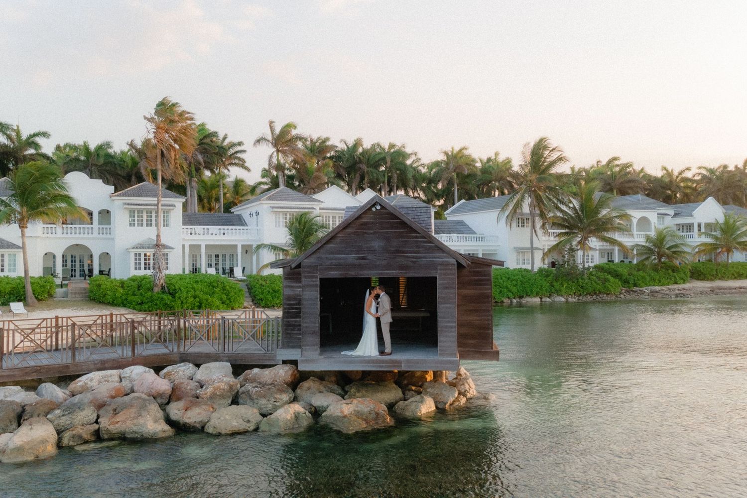 A married couple at Half Moon Montego Bay Resort photograped kissing next to the water at sunset, by PhotoMagic Studio