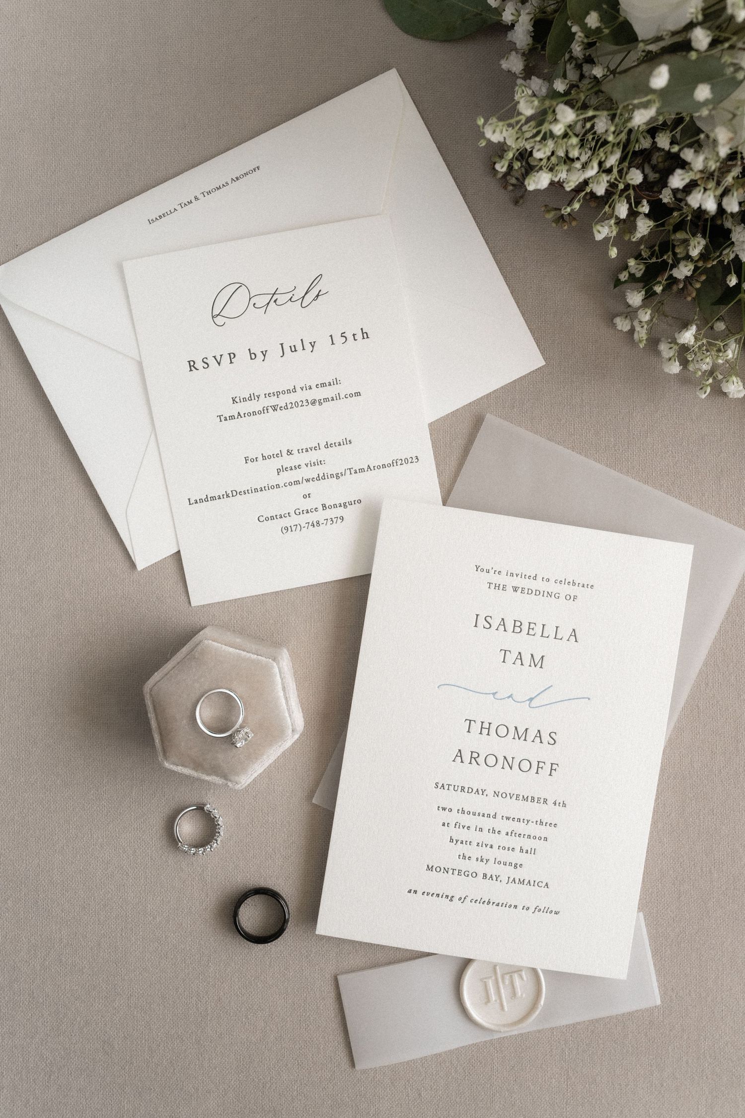 Minimalist wedding invitation suite with rings and wax seal on gray background with baby's breath flowers.