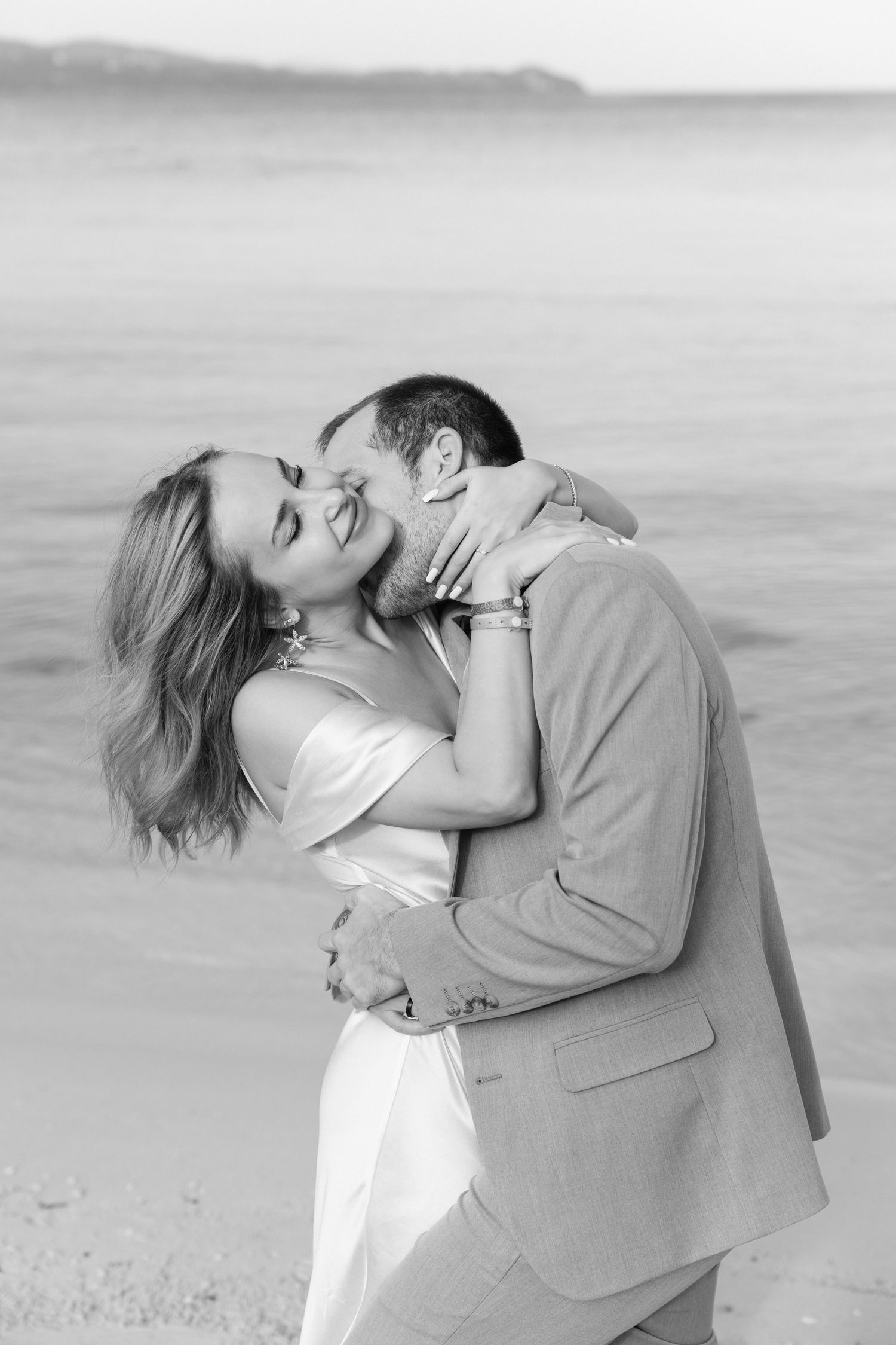 Black and white portrait of a romantic beach wedding embrace with ocean in background.