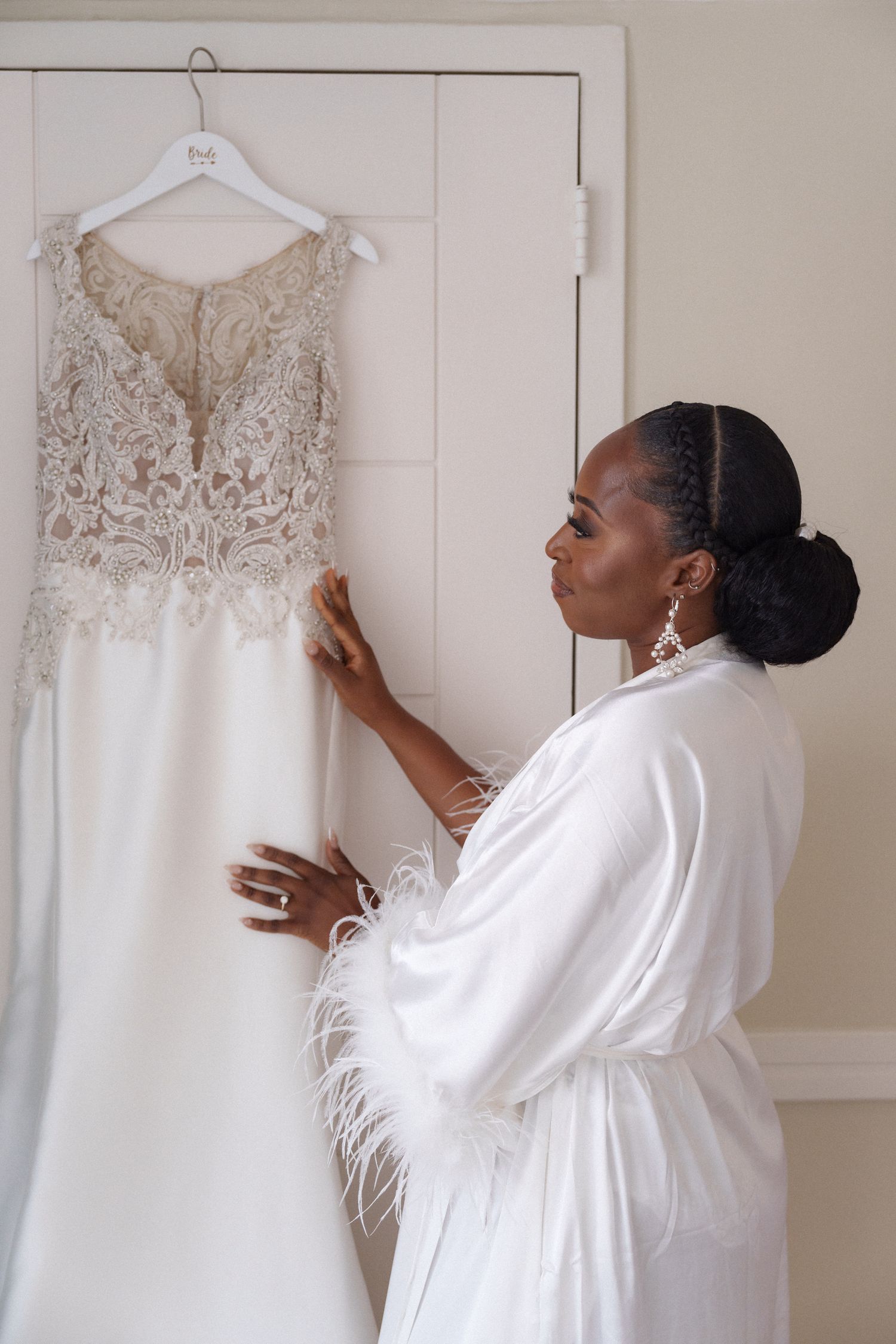 A bride in a white robe admiring her lace wedding dress hanging on display.
