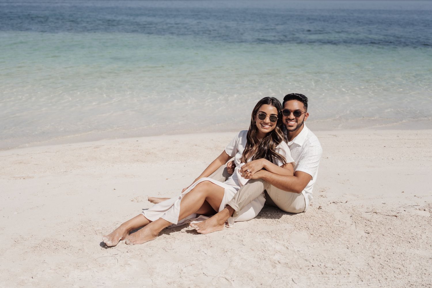 A couple sitting together on white sand beach enjoying a romantic moment.