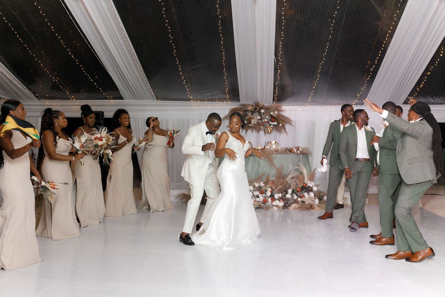 Wedding guests dancing and celebrating under a white tent decorated with string lights.
