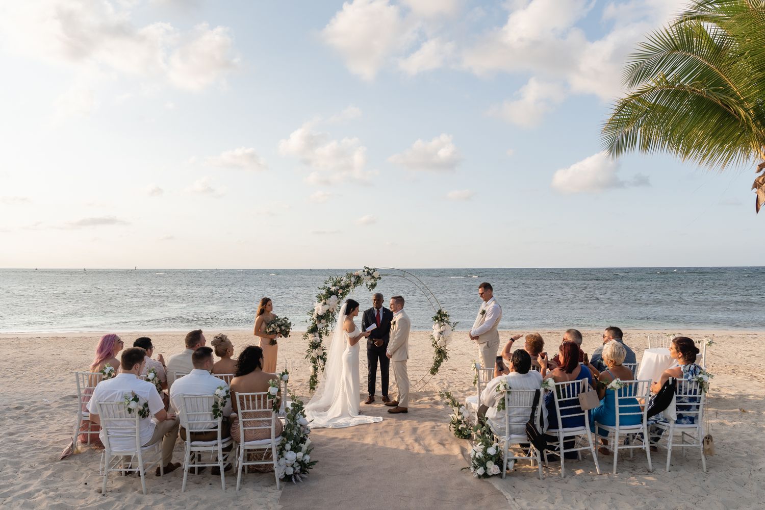 Intimate beach wedding ceremony with guests seated in white chairs facing the ocean.