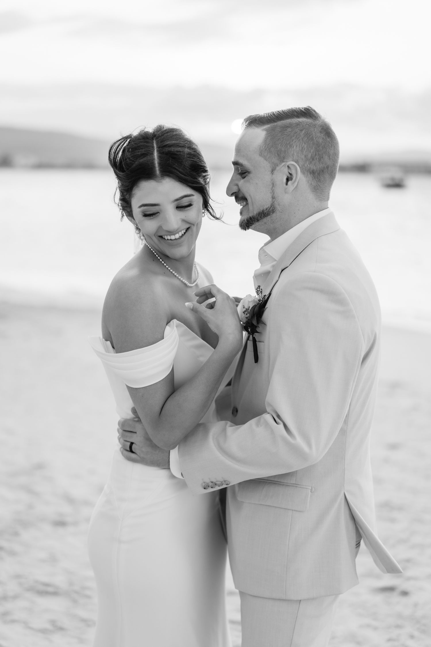 A romantic wedding couple embraces on a beach in black and white photography.