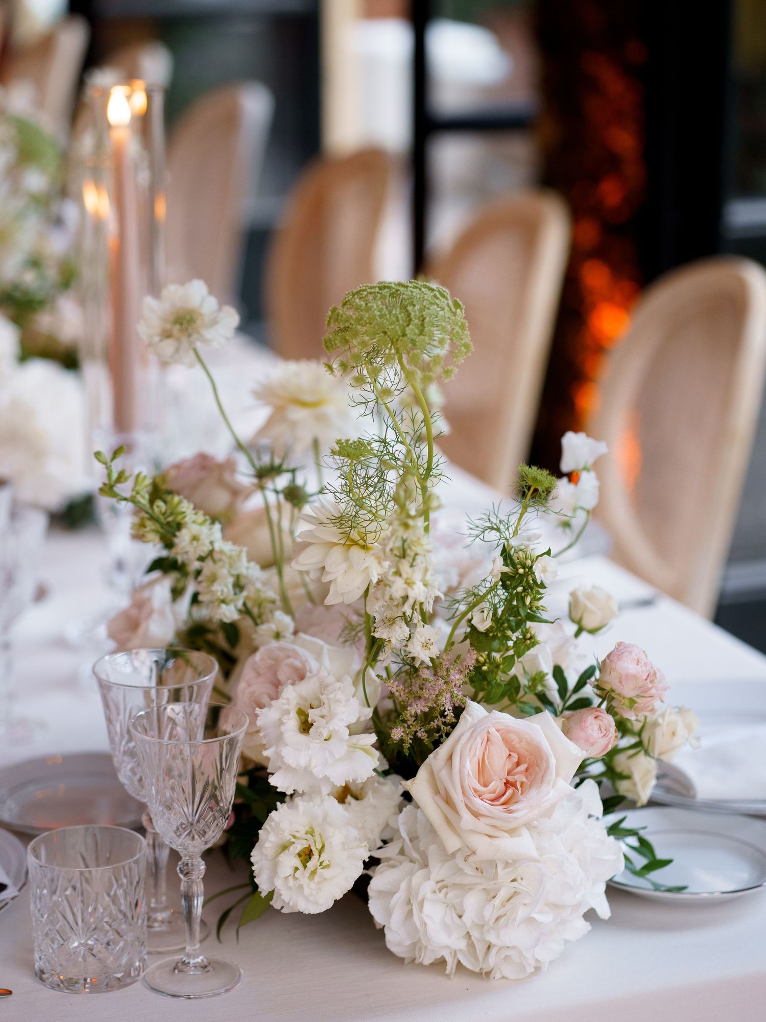 Romantic wedding table setting with delicate pink and white floral centerpieces and crystal glassware.
