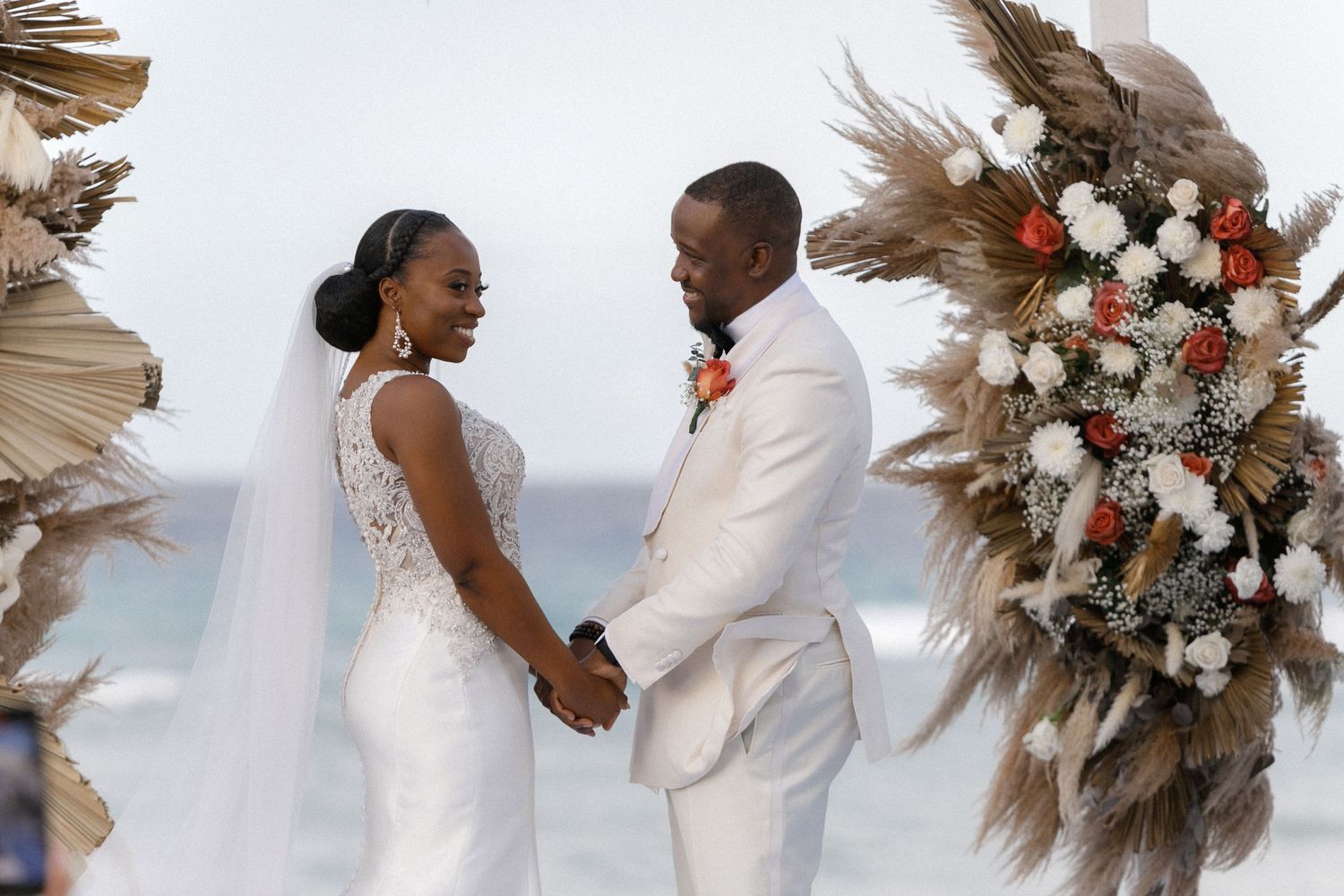 Wedding couple sharing a joyful moment under a beautiful floral arch with pampas grass.