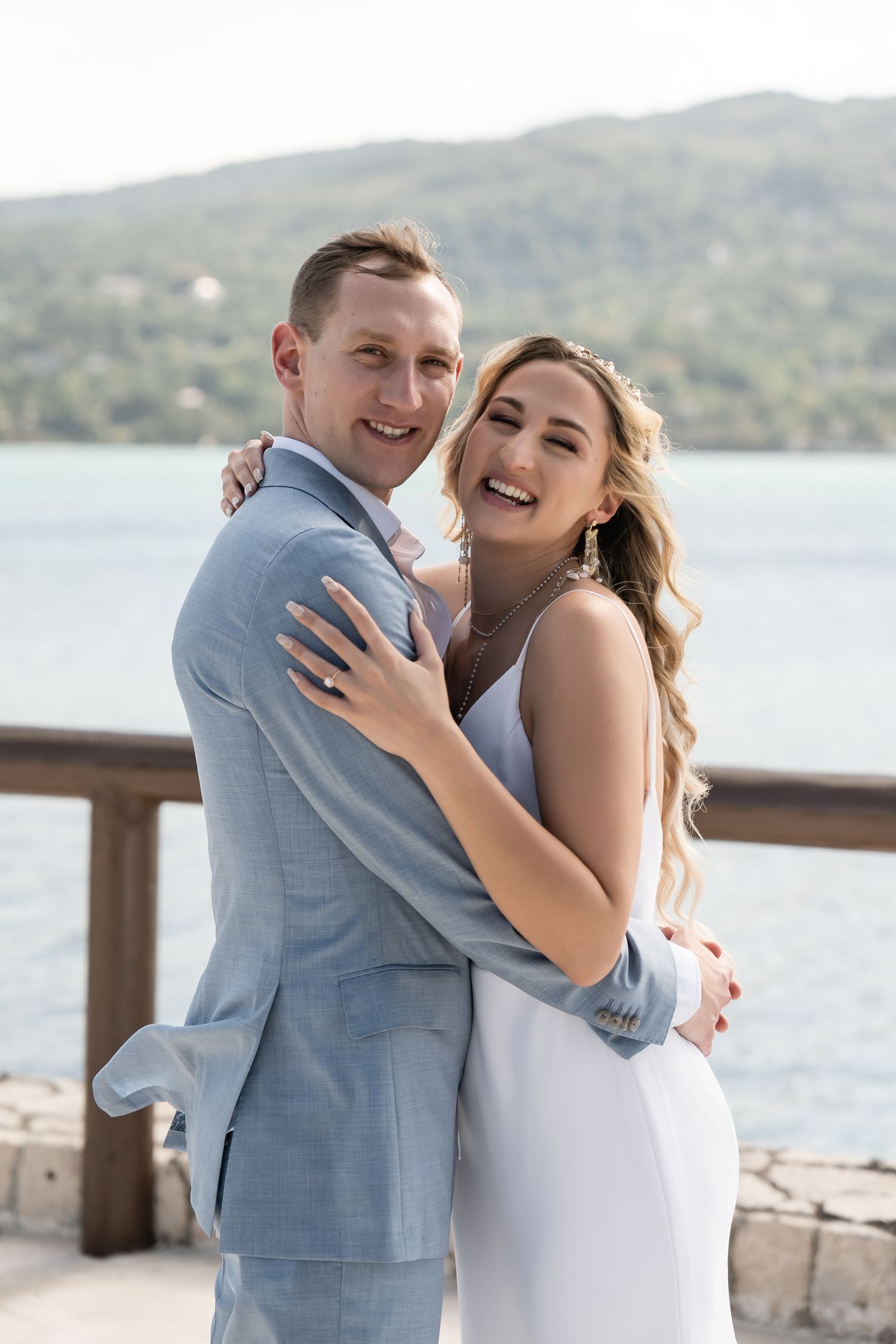 A joyful wedding portrait on a scenic overlook with water and mountains behind.