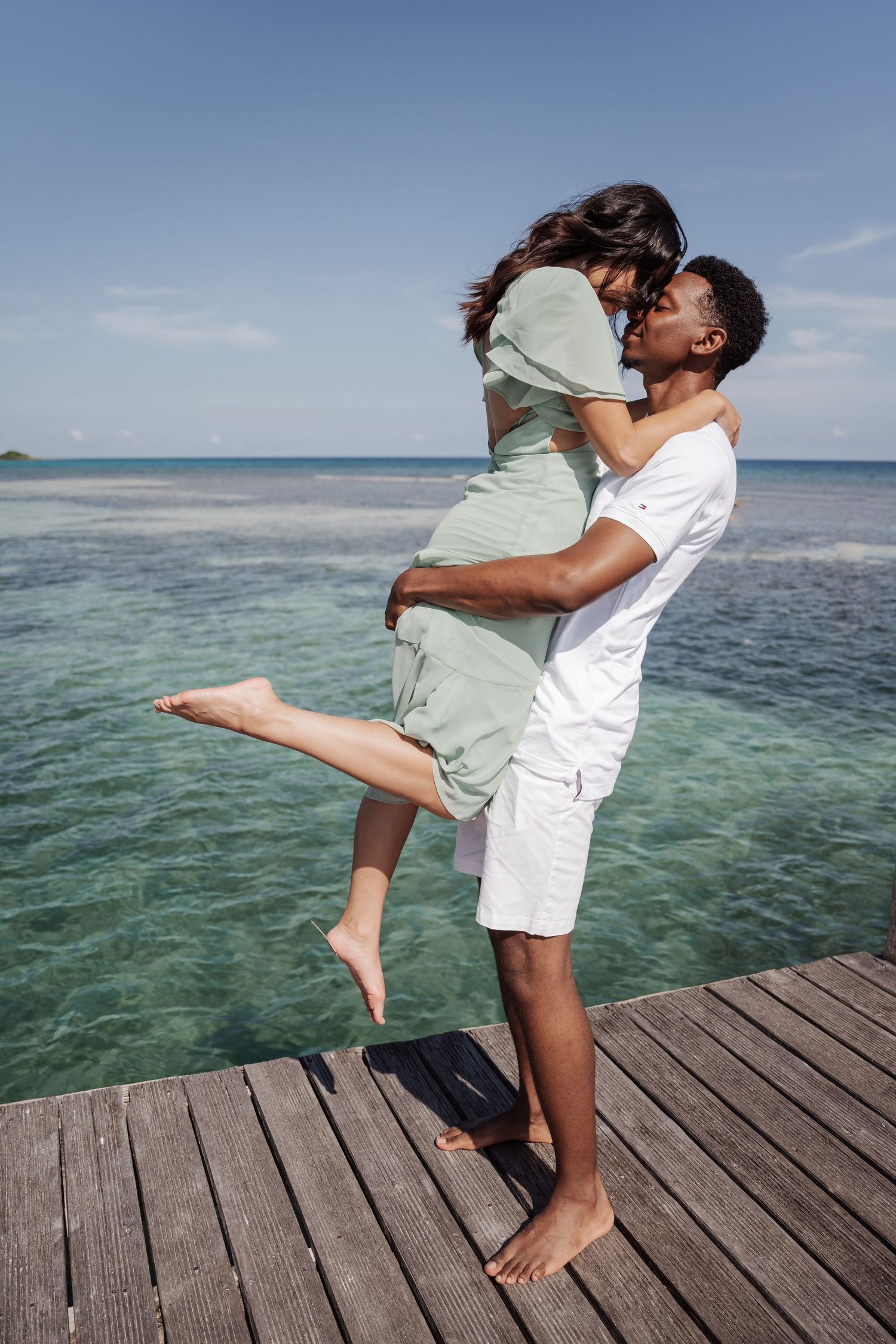 A joyful lift pose on a wooden dock with turquoise waters in the background.