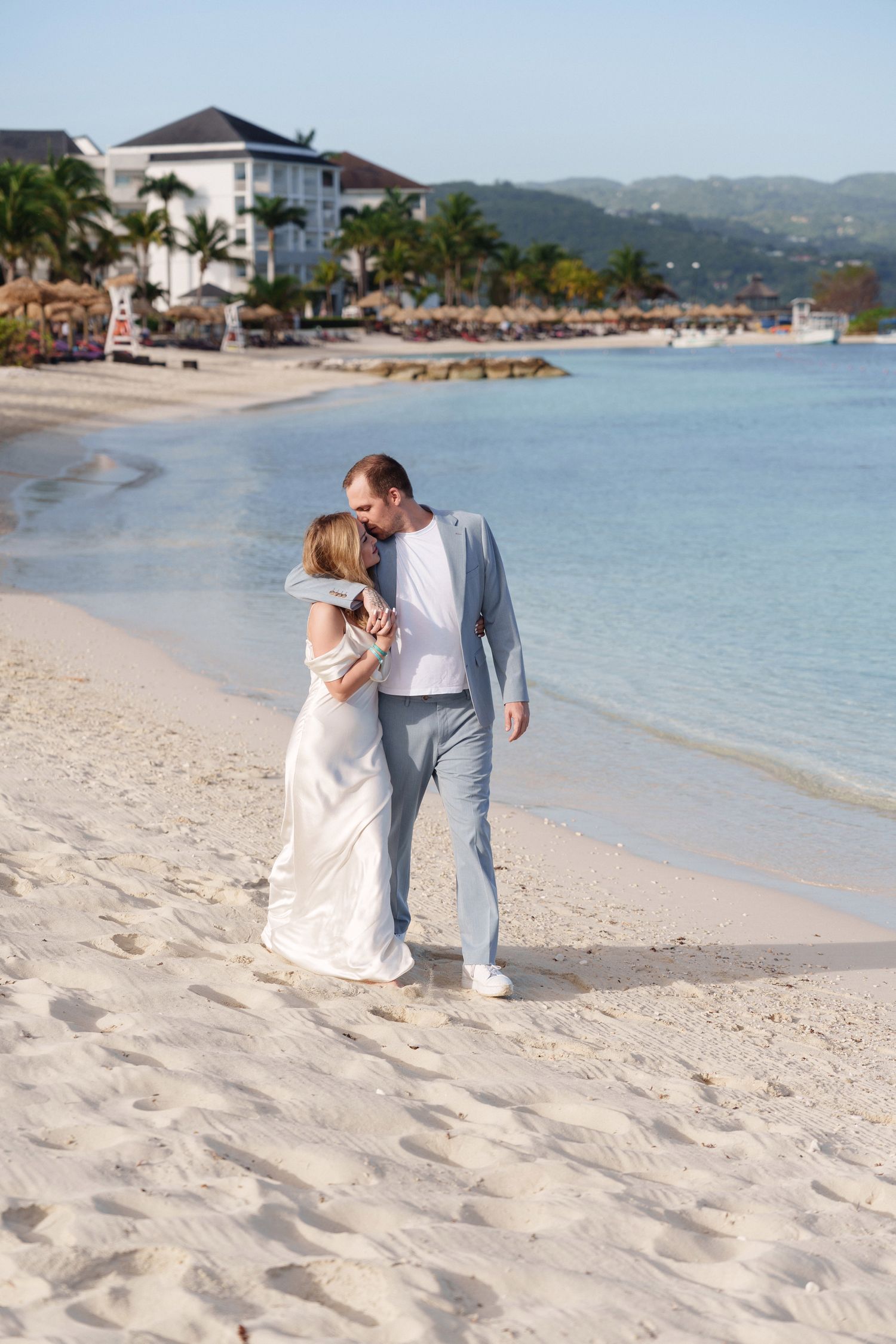 Beachfront wedding photo with palm trees and resort buildings in the background.