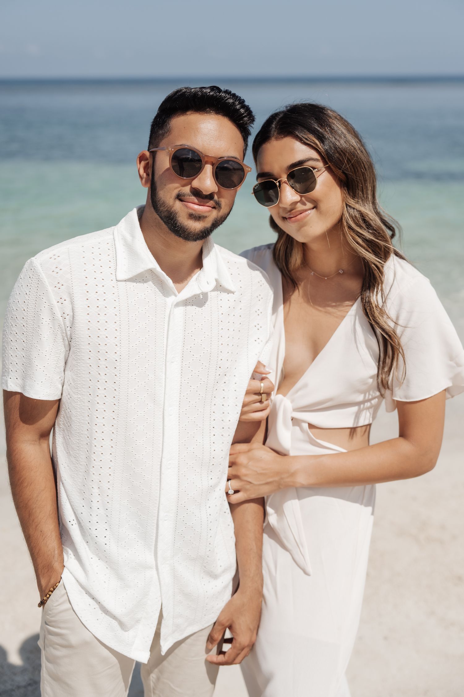 Stylish couple in white outfits poses on beach.