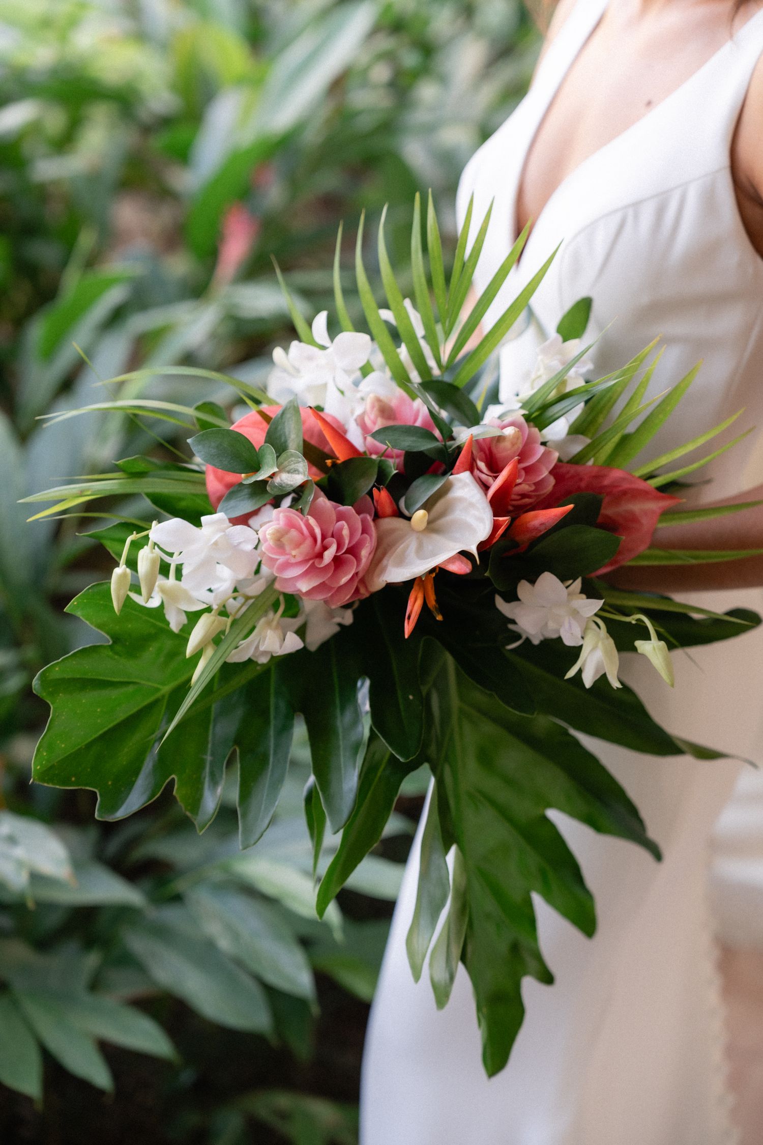 Tropical wedding bouquet with pink roses, white flowers and large green leaves.