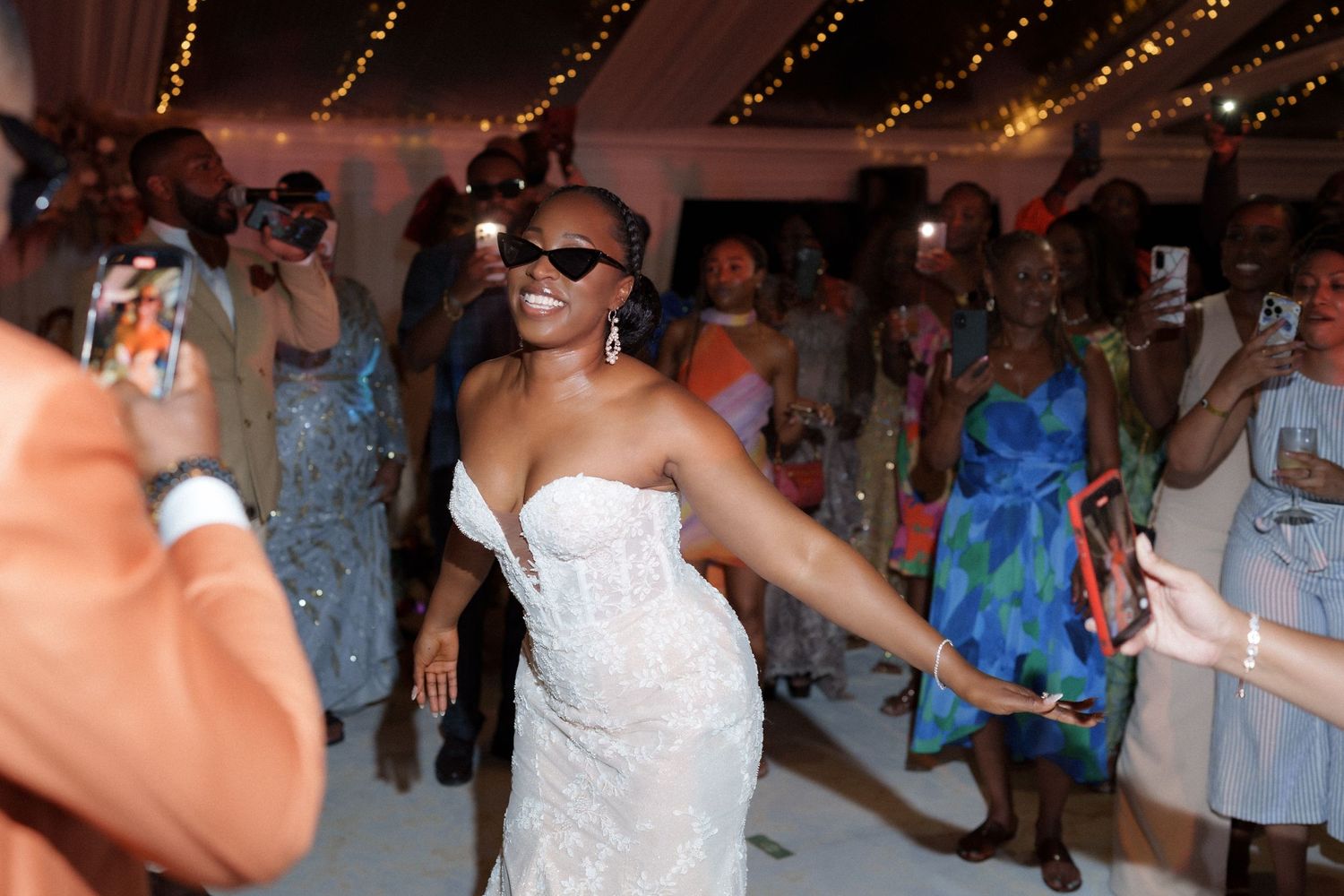 Joyful dance celebration at wedding reception with guests watching and taking photos.