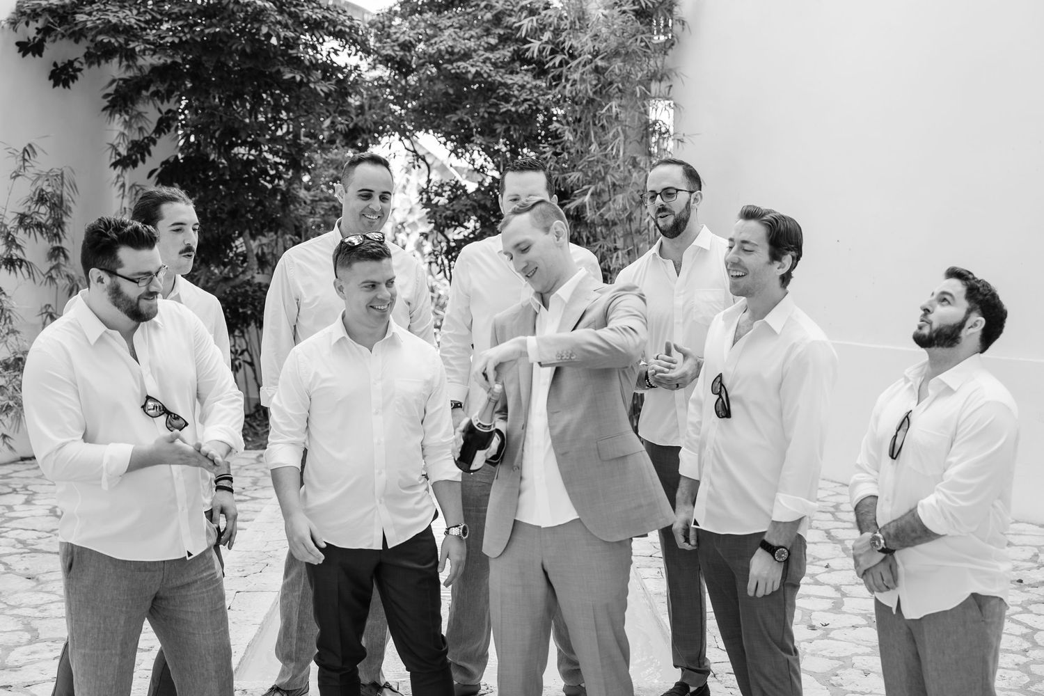 Groomsmen in white shirts and gray pants sharing laughs during outdoor wedding photoshoot.