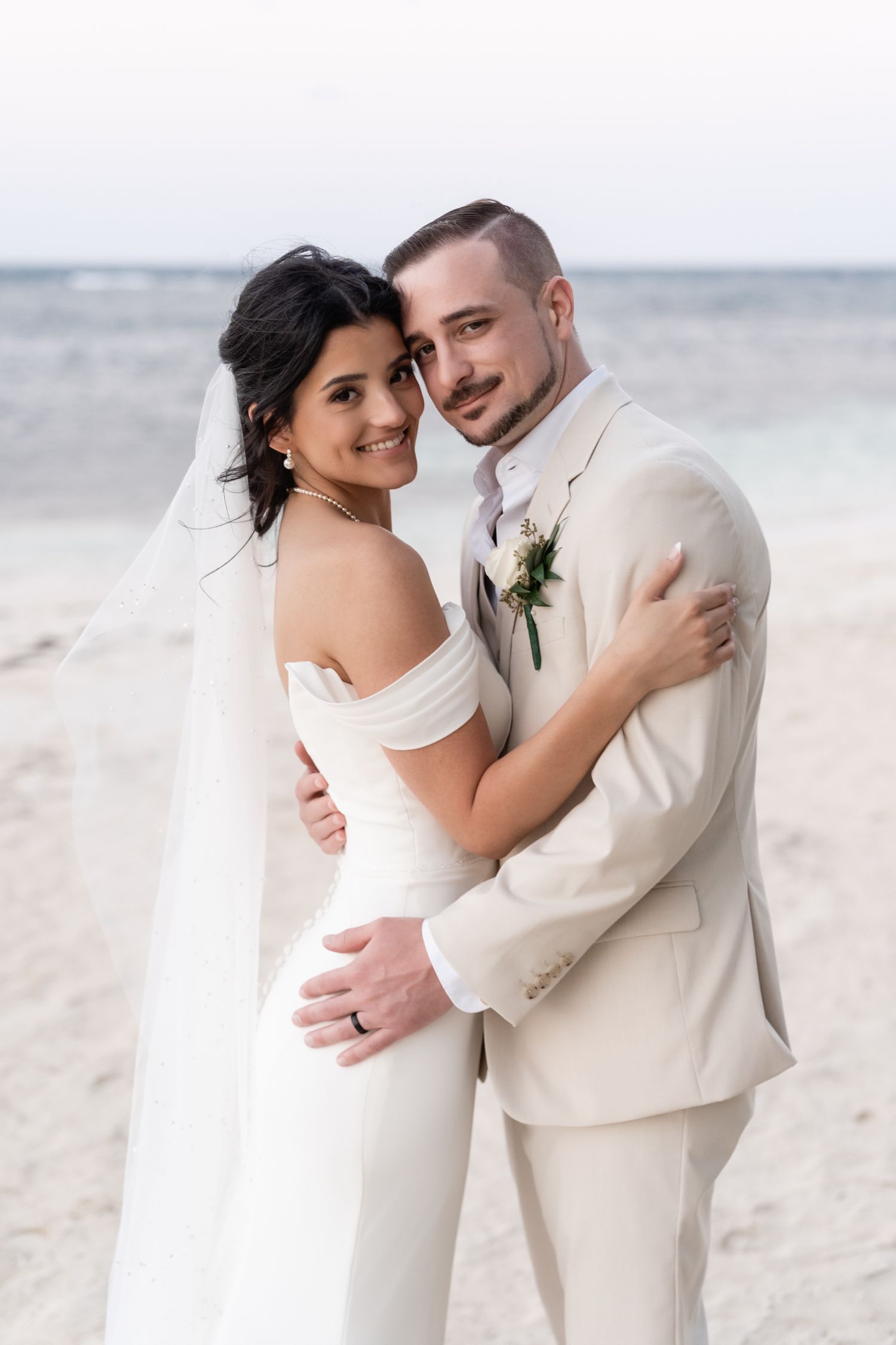 A romantic beach wedding portrait features a couple in elegant white attire against the ocean backdrop.