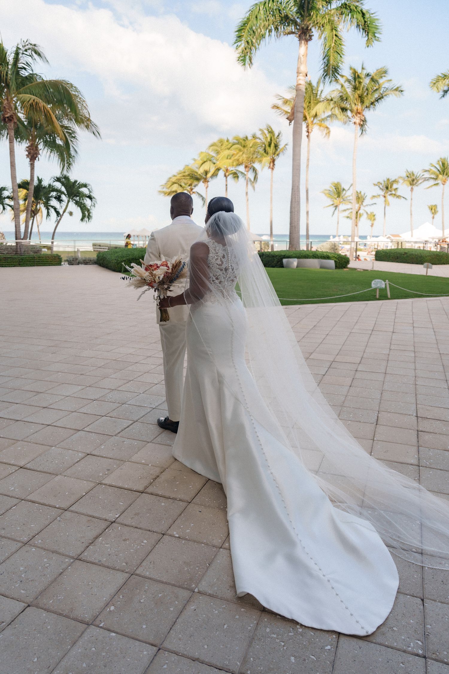 Newlyweds walking along a palm-tree lined tropical venue after their wedding ceremony.