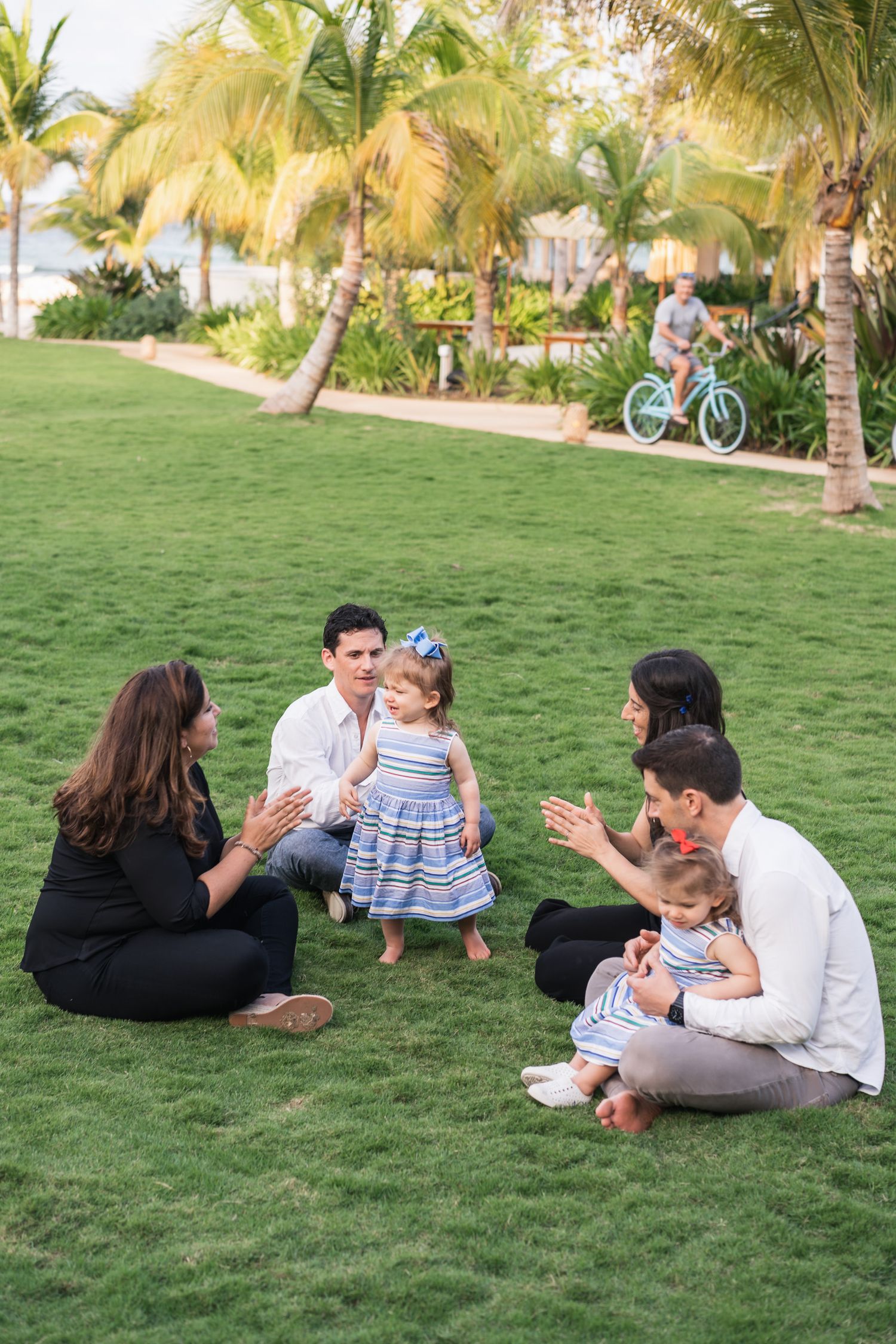 Family gathering on a lush green lawn surrounded by palm trees at a tropical resort.