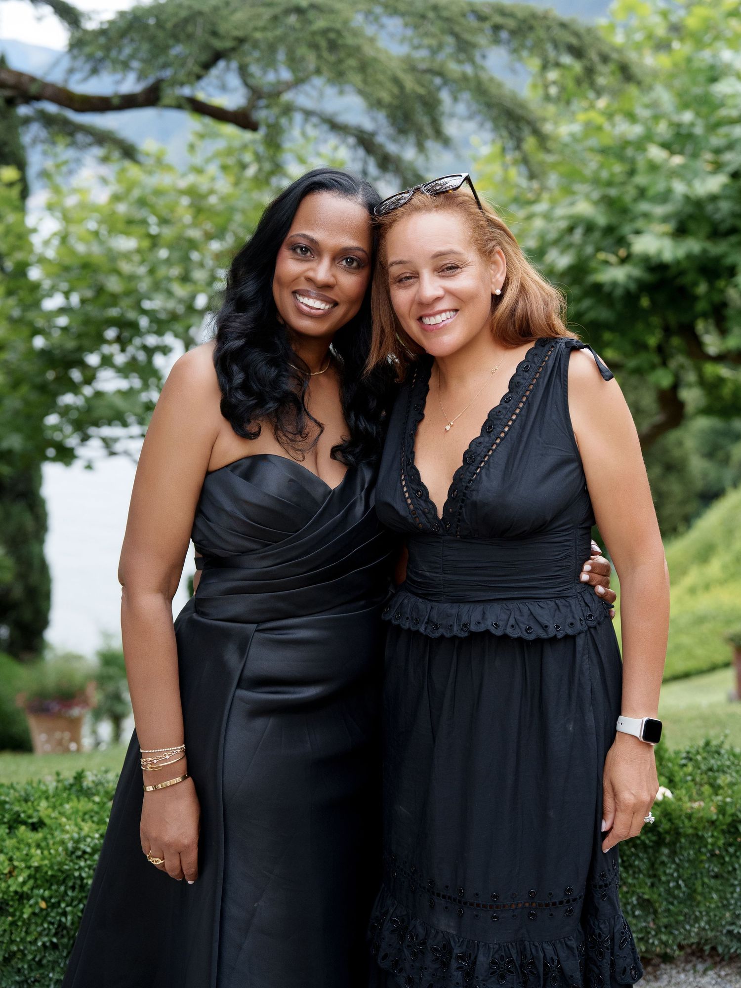 Wedding attendants in black dresses pose together outdoors in a garden setting.