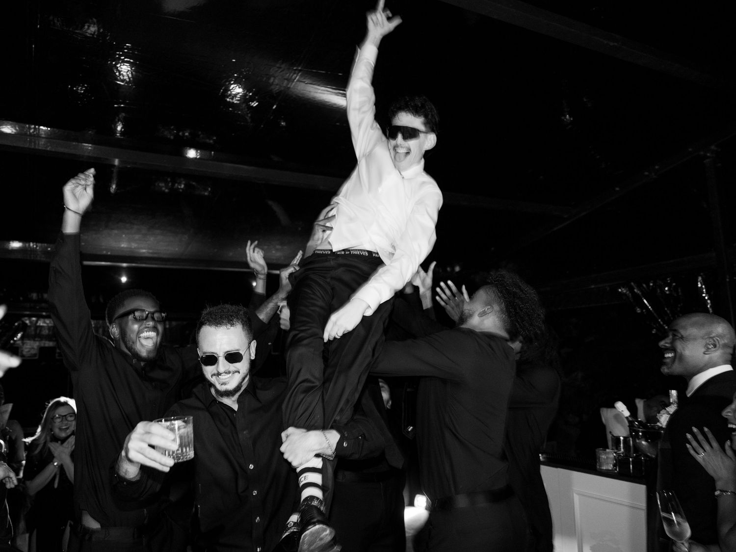 Party guests dancing and celebrating at a nightclub with dramatic black and white lighting effects.
