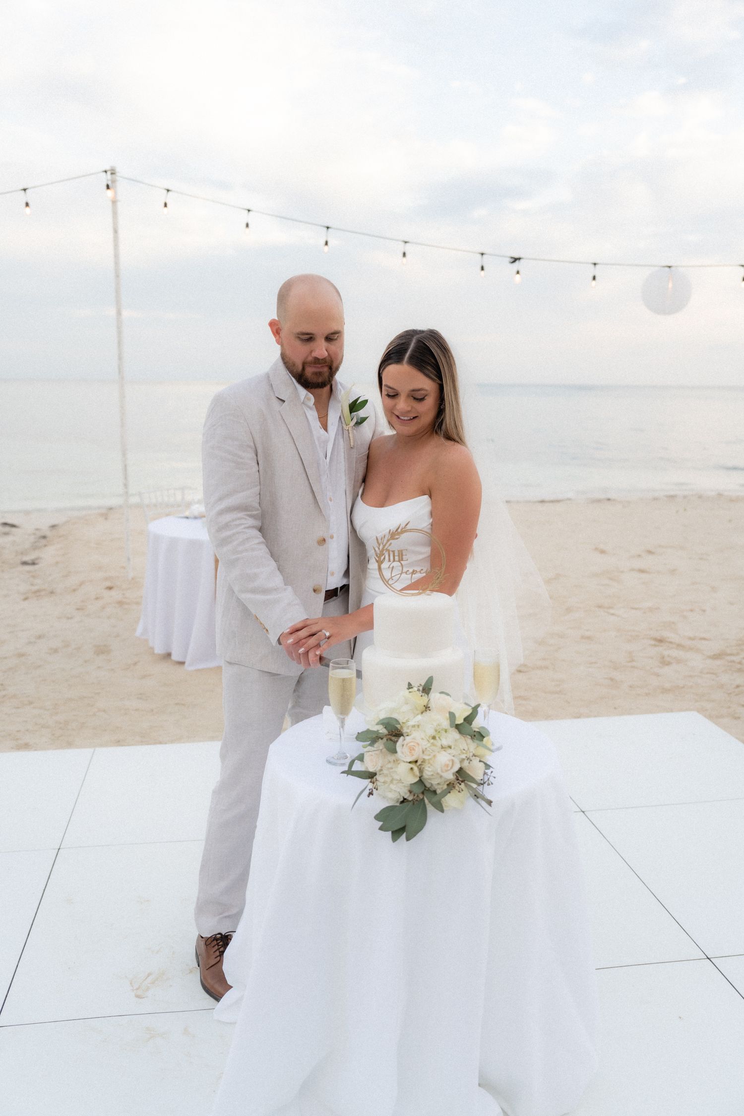 Beach wedding couple on white dance floor with string lights overhead.