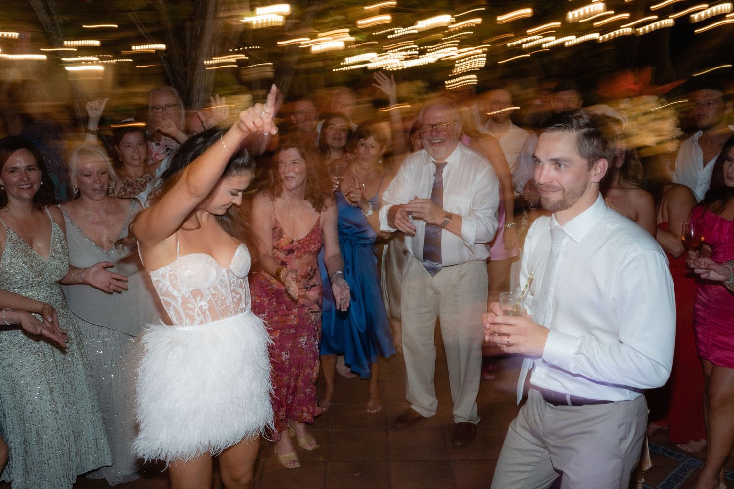 Wedding guests dance and celebrate on illuminated dance floor at reception.