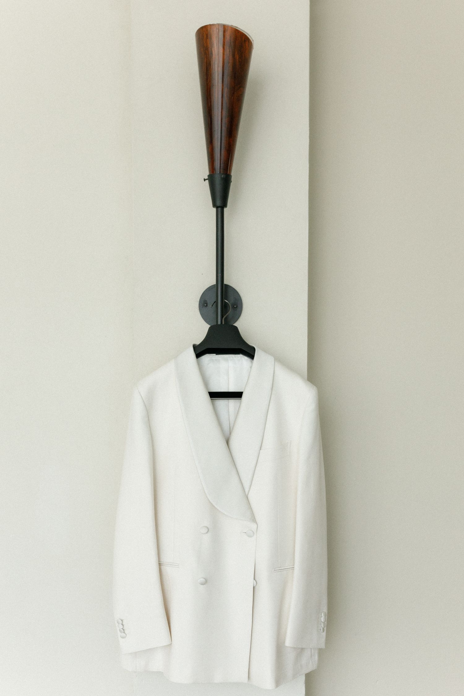 Crisp white wedding tuxedo jacket hanging on wooden wall-mounted coat hook.