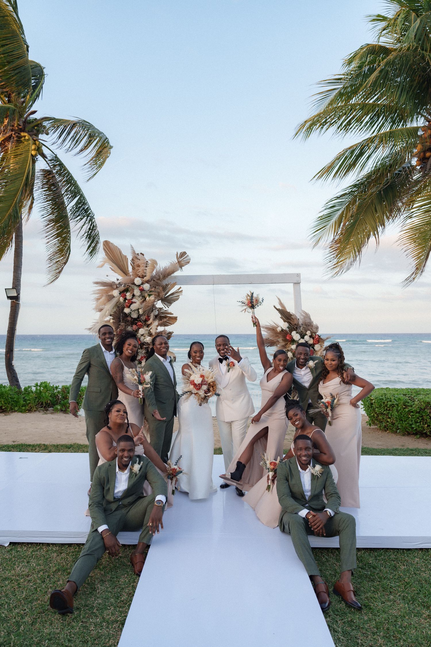 Wedding party in coordinated outfits poses on beachfront white platform with tropical decor.