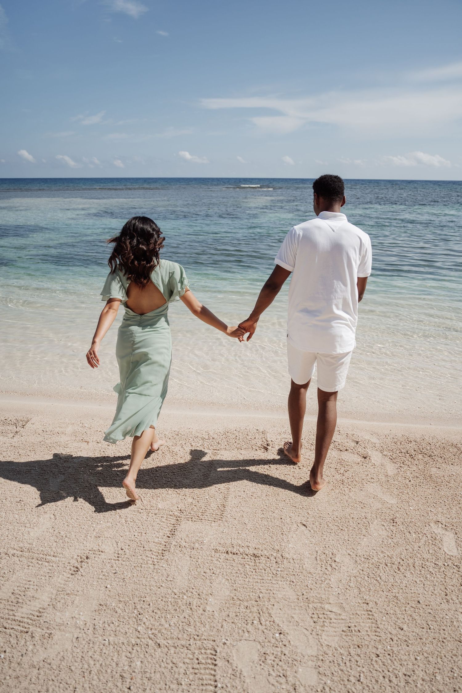 A couple walks hand in hand along a pristine beach with crystal clear waters.