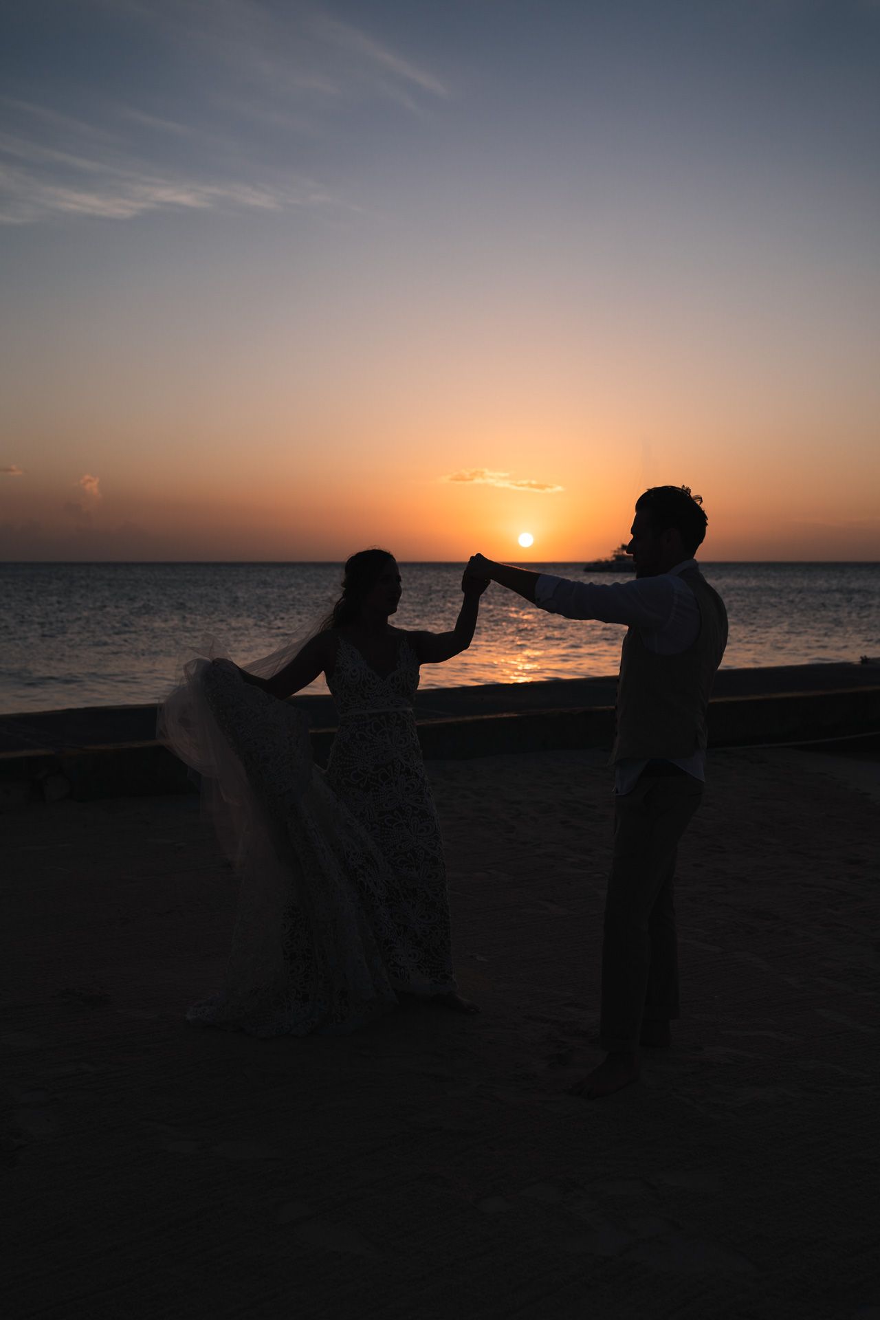 Silhouettes of a dancing couple against an ocean sunset.